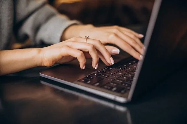 Person typing on a laptop keyboard with a dark wooden surface.