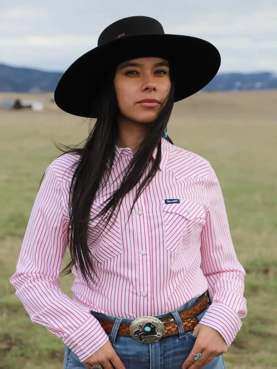 A portrait of Katie Fire Thunder standing in Montana range land looking at the viewer.