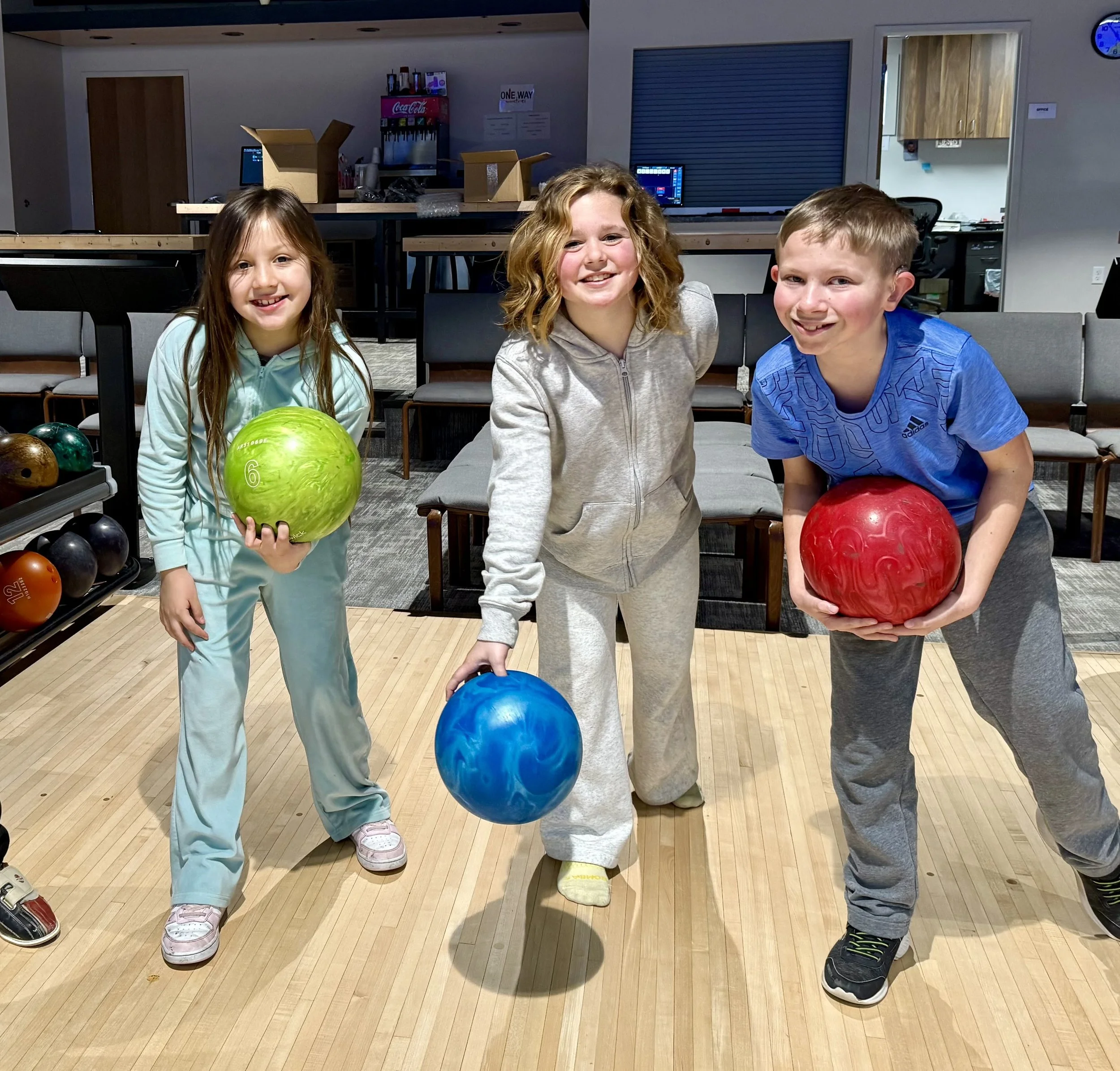 Three kids smiling and holding bowling balls