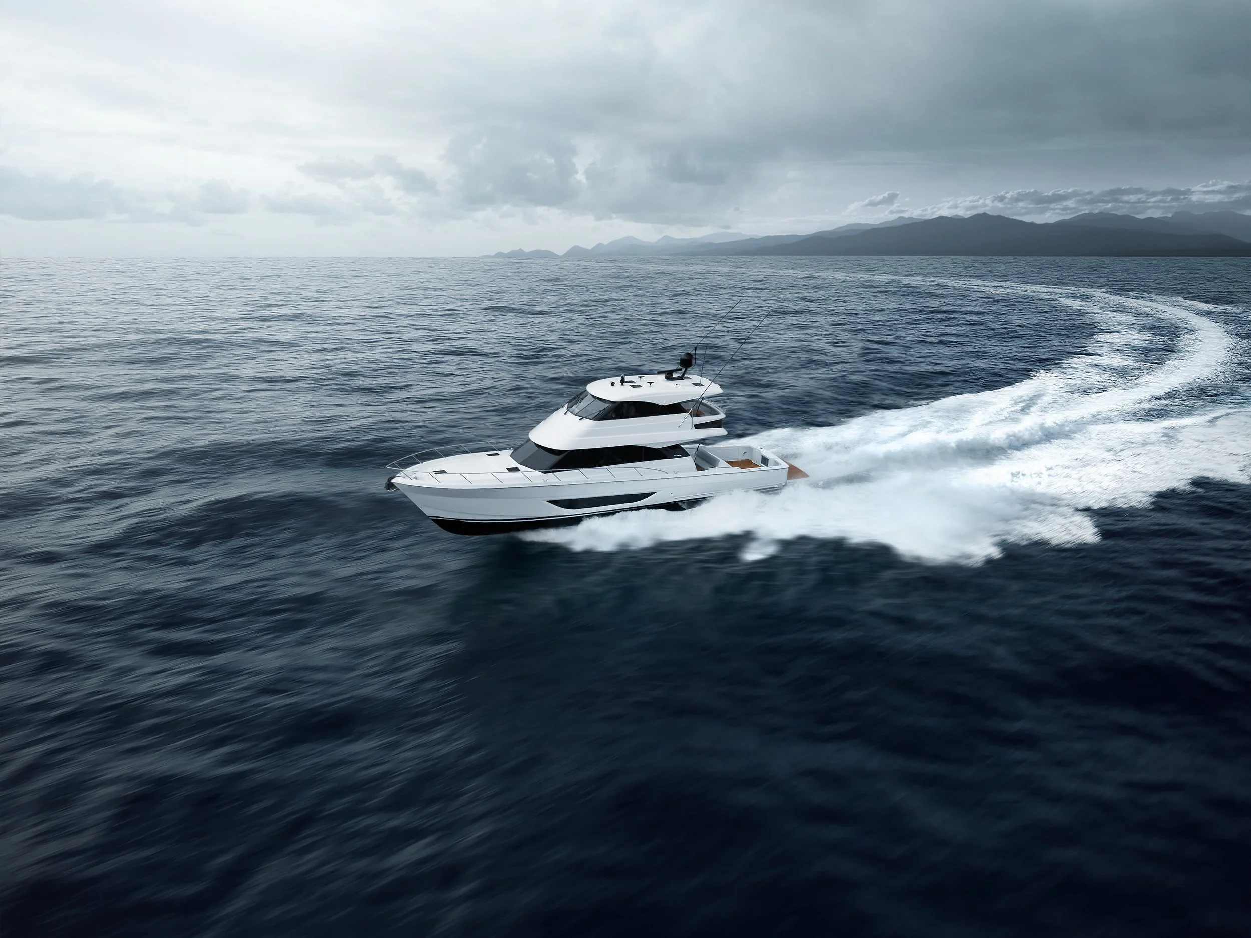 A white yacht speeding across the open sea, leaving a wake behind it, with mountains and a cloudy sky in the background.