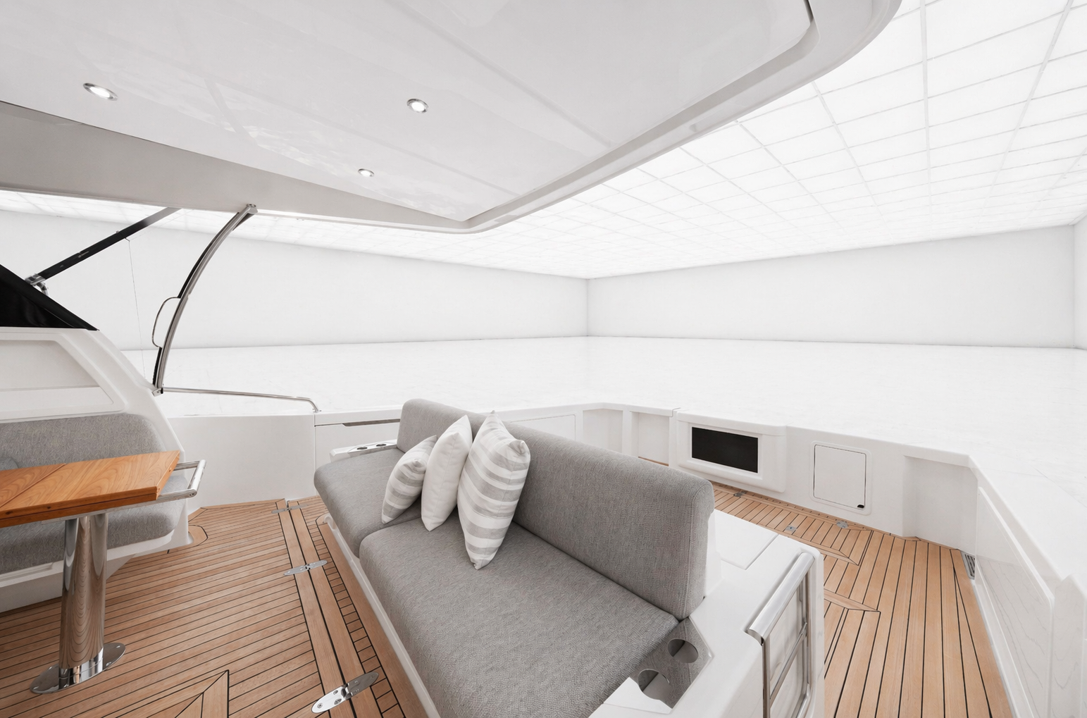 Interior of a luxury yacht with white walls, wooden deck, gray sofa with pillows, and a small wooden table.