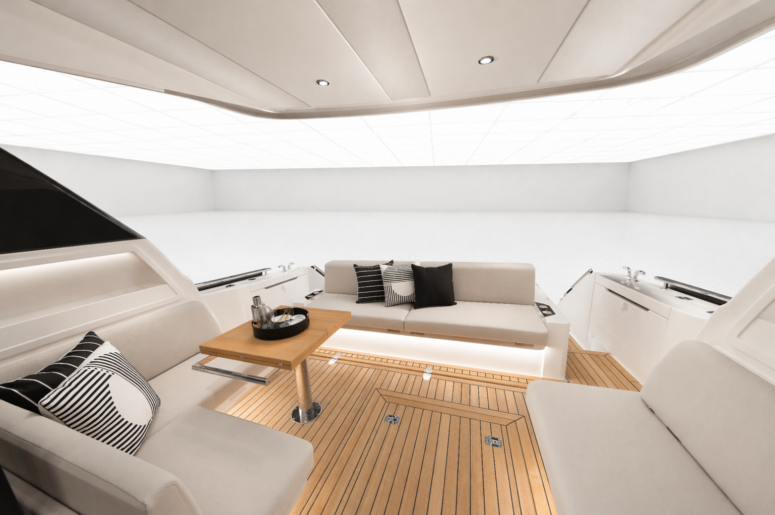 Interior of a modern, minimalist yacht with white cushioned seating, black and white striped pillows, a small wooden table with drinks and glasses, and light wooden flooring.