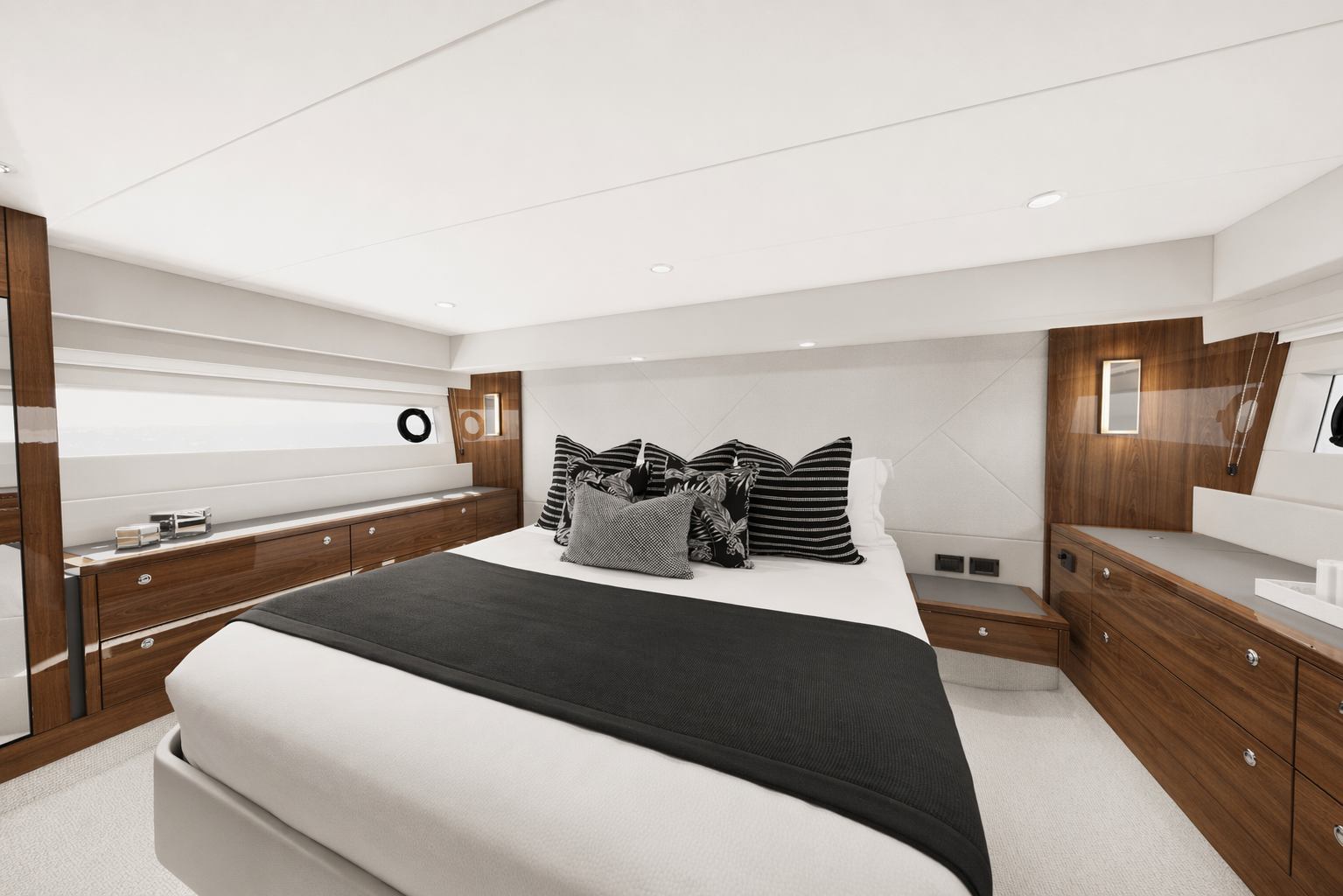 Modern bedroom with white walls and ceiling, a large bed with black and patterned pillows, and wooden furniture along the walls.