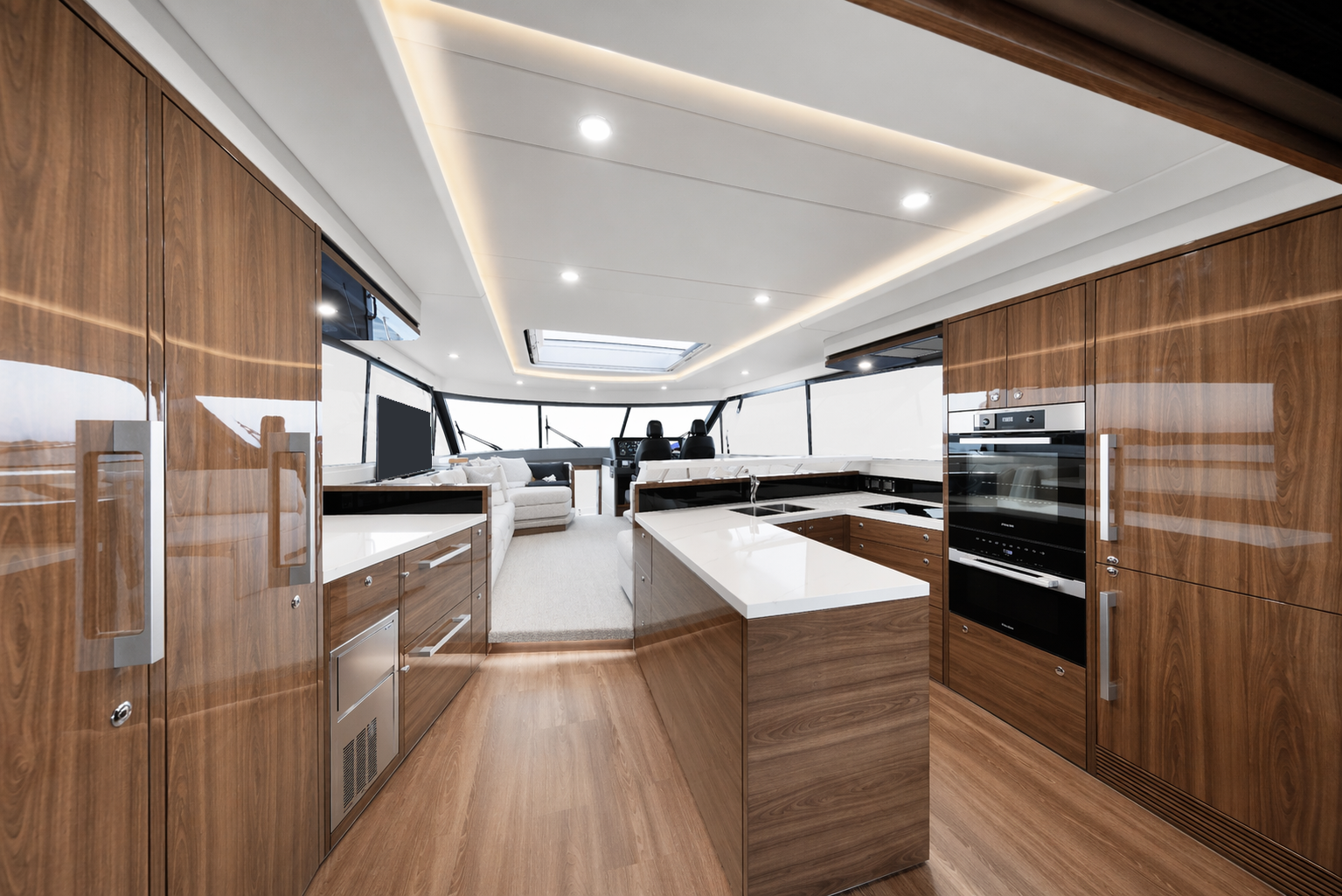 Modern yacht interior with wooden cabinetry, white countertops, and a view of the living area with a sofa and captain's chairs.