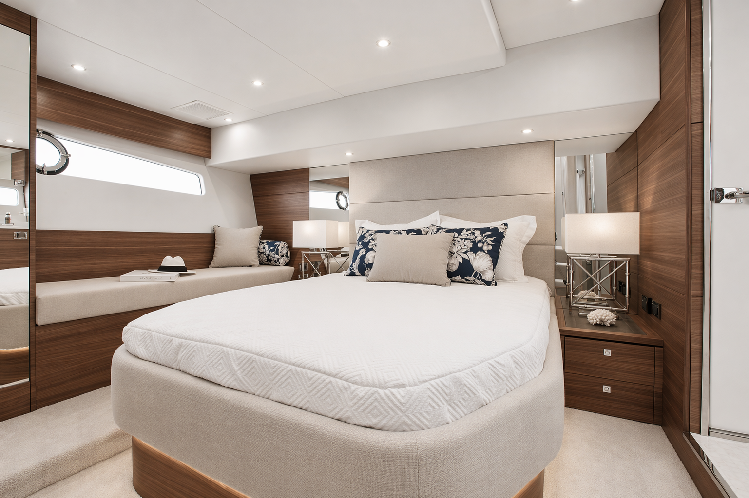 Interior of a modern bedroom with a bed, nightstands, lamps, and a side seating area, featuring wood paneling and neutral tones.