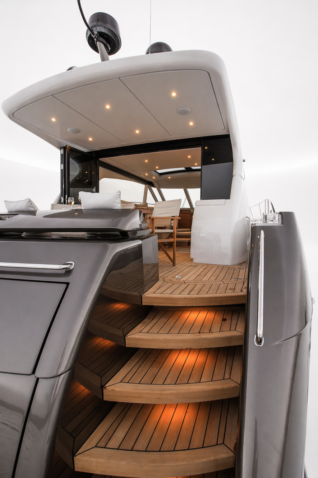 The image shows the exterior of a luxury yacht with a wooden deck, stairs leading up to an open-air seating area with white cushions, and a covered upper deck with seating and lighting.