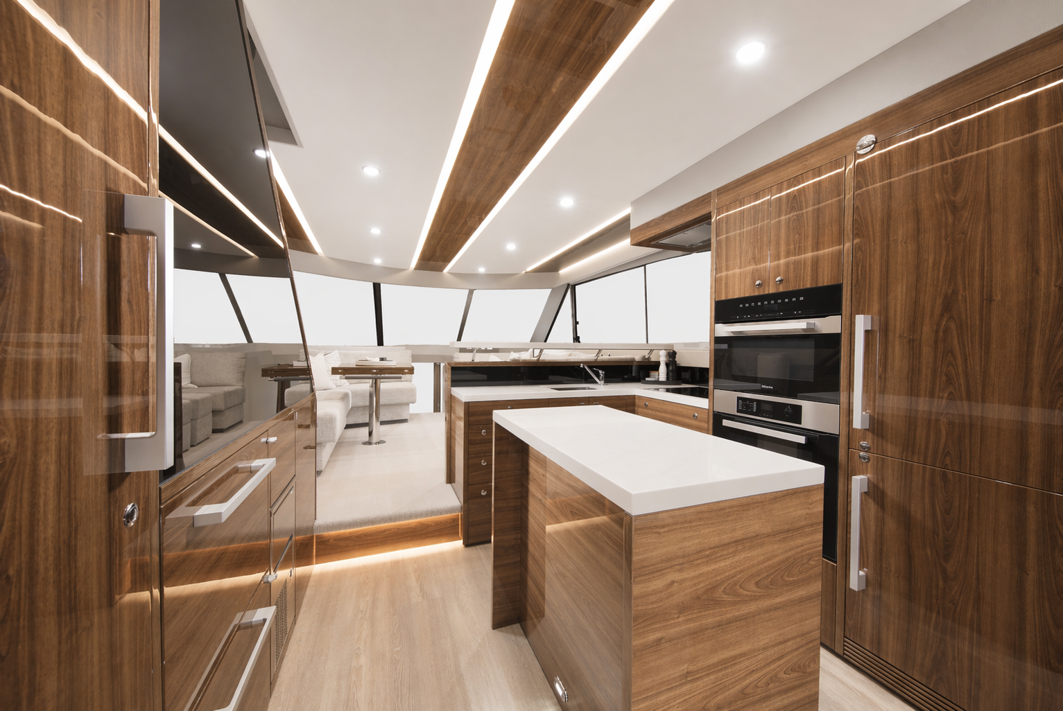 Modern kitchen with wood cabinets, white countertops, and built-in appliances, overlooking a living area with sectional sofa near large windows.