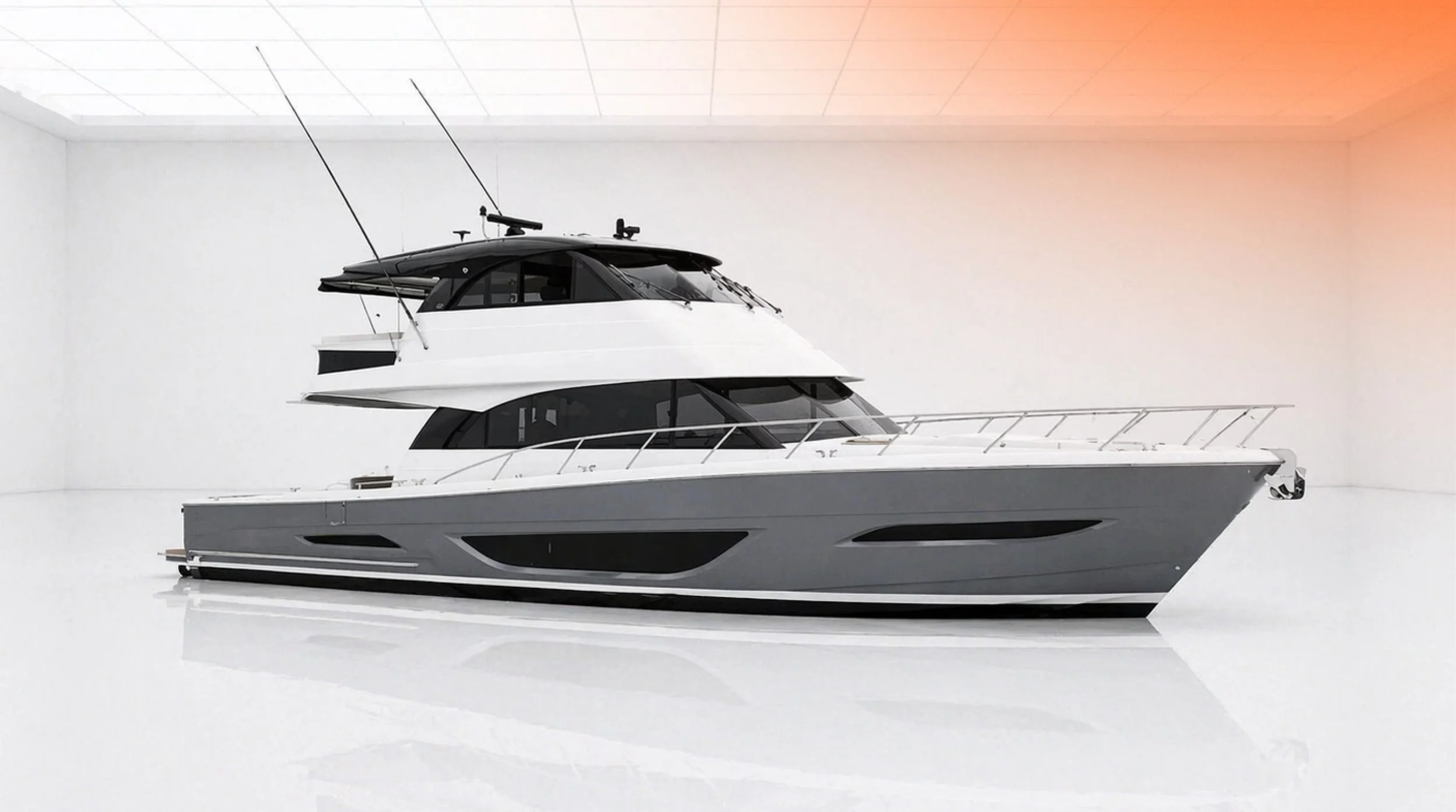 A modern luxury yacht with multiple decks, white and black exterior, and antennas, inside a white room with ceiling grid and a warm light on the right.