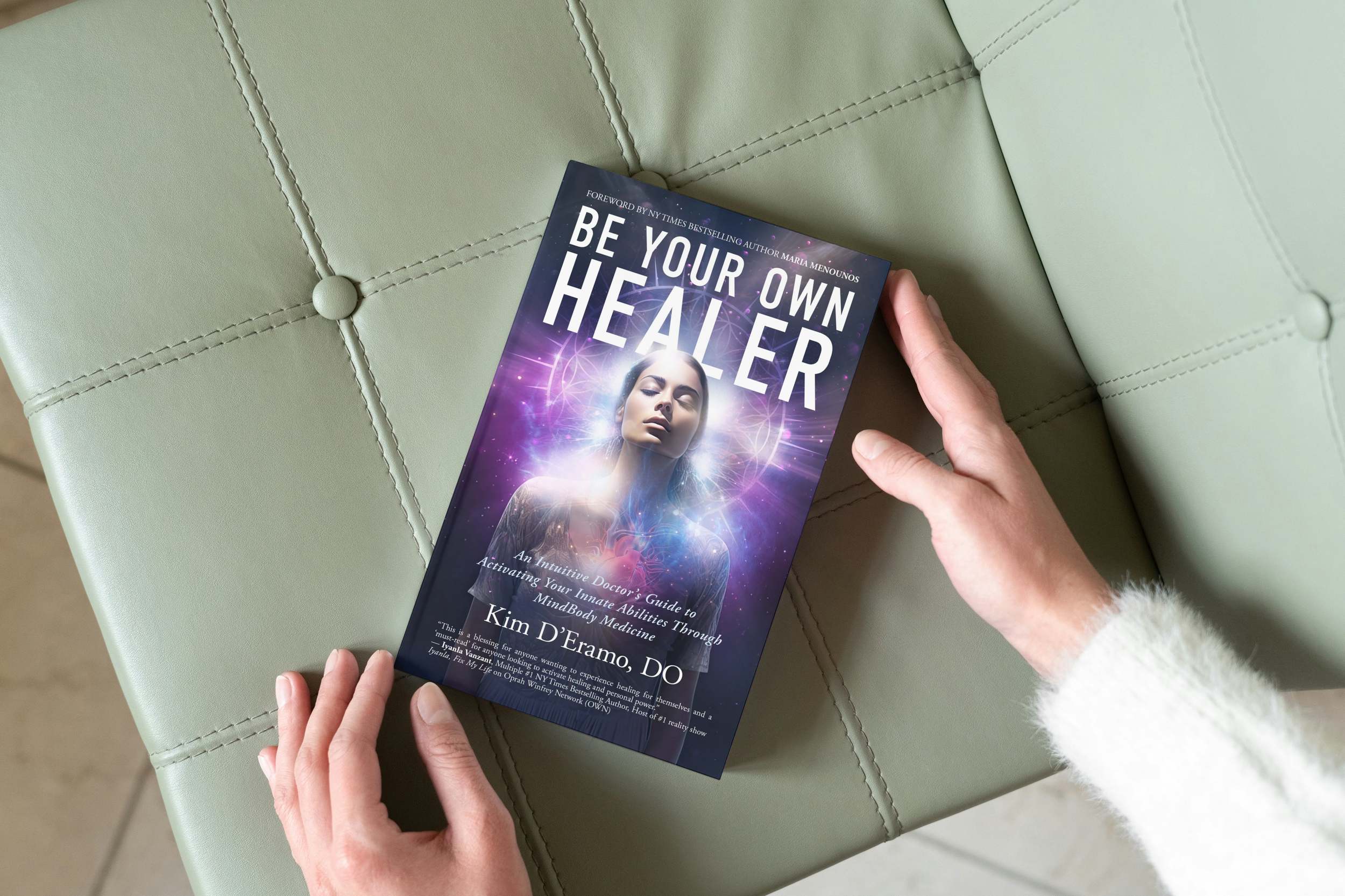 Two hands hold open a copy of Be Your Own Healer, resting on a sage green surface.
