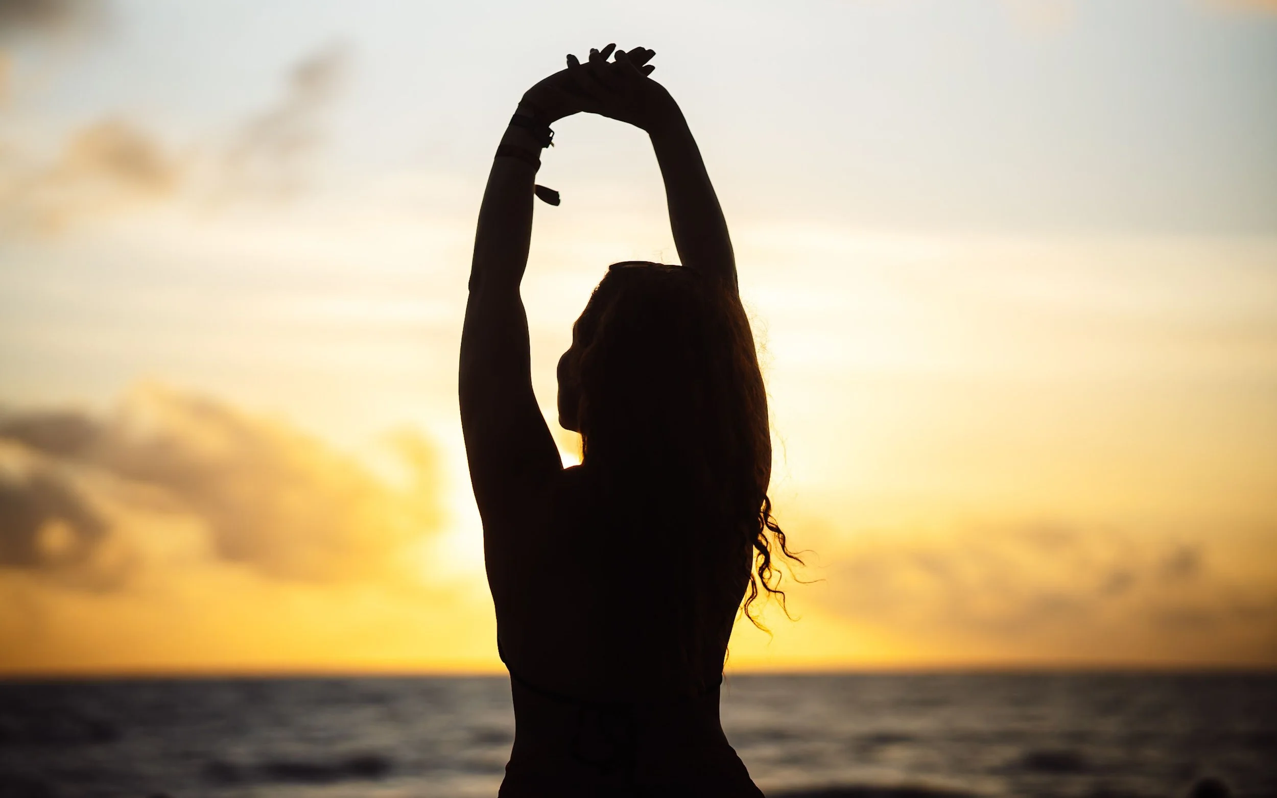 Silhouette of woman stretching by the ocean under a vibrant sunset.