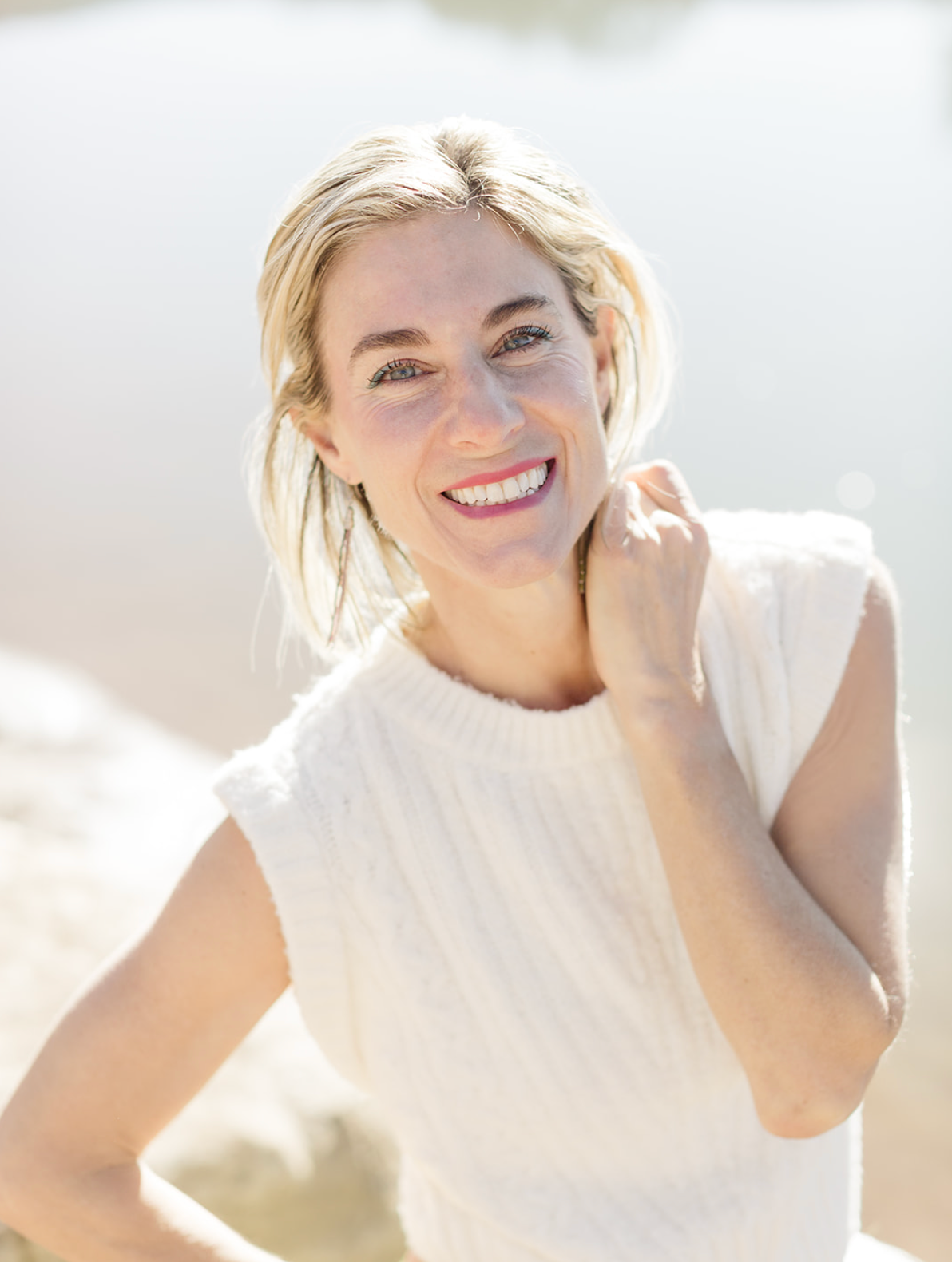 Dr. Kim laughs warmly in bright, airy light, wearing a white cable-knit sleeveless top, her hand resting lightly at her neck.