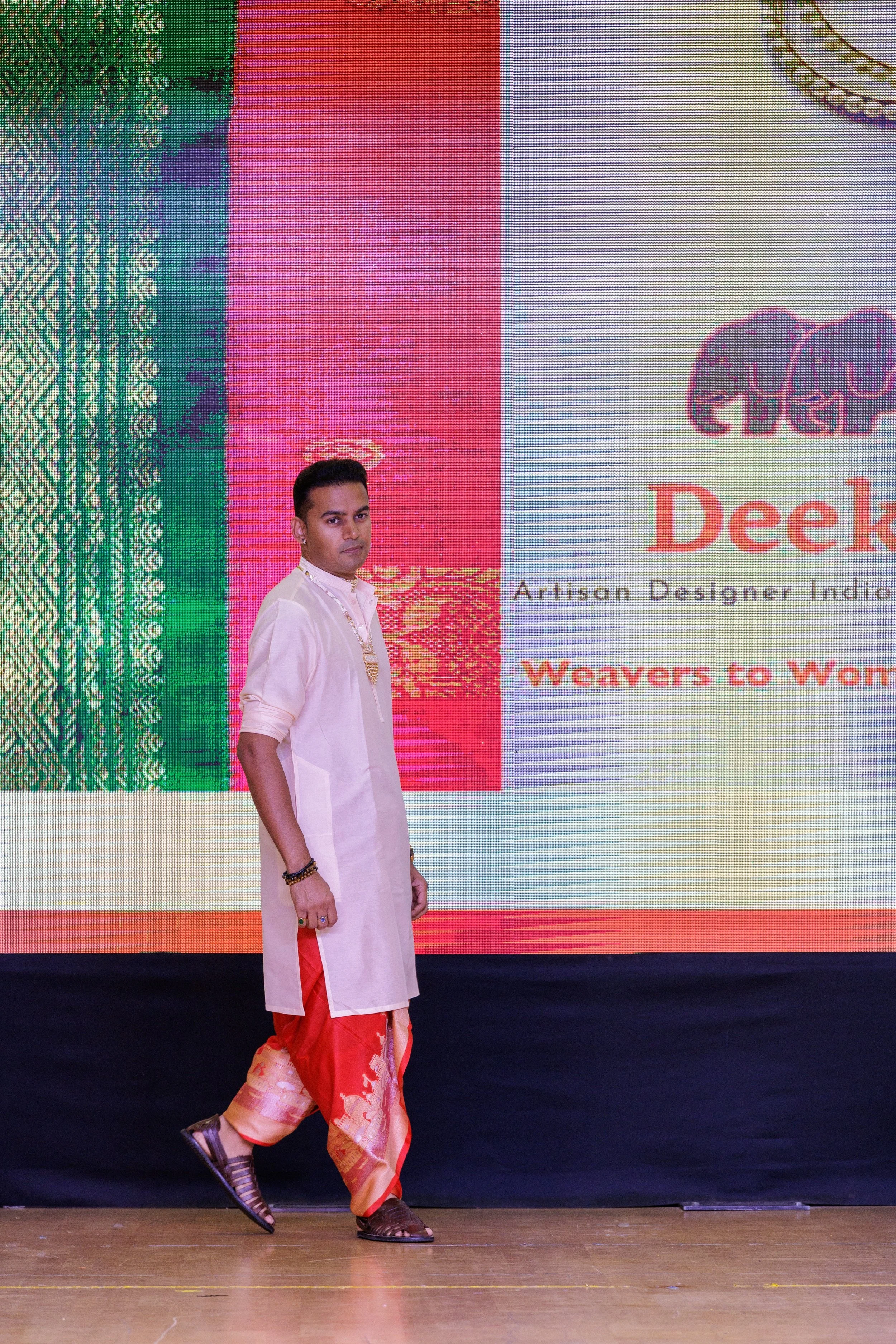 A man dressed in traditional Indian attire walking on a stage with a colorful digital backdrop behind him.
