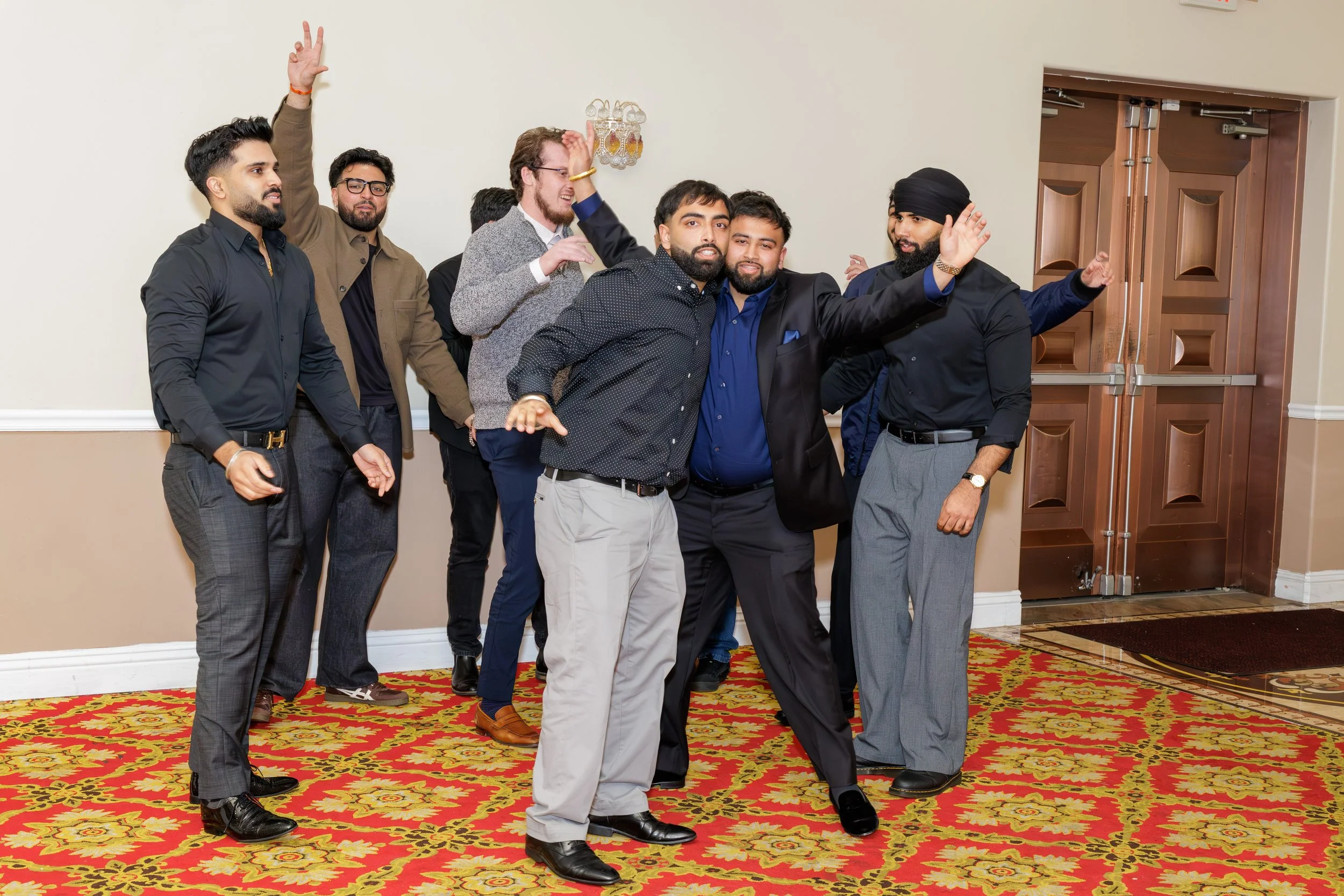 A group of men dancing and celebrating indoors, with a wooden door in the background and a colorful patterned carpet.