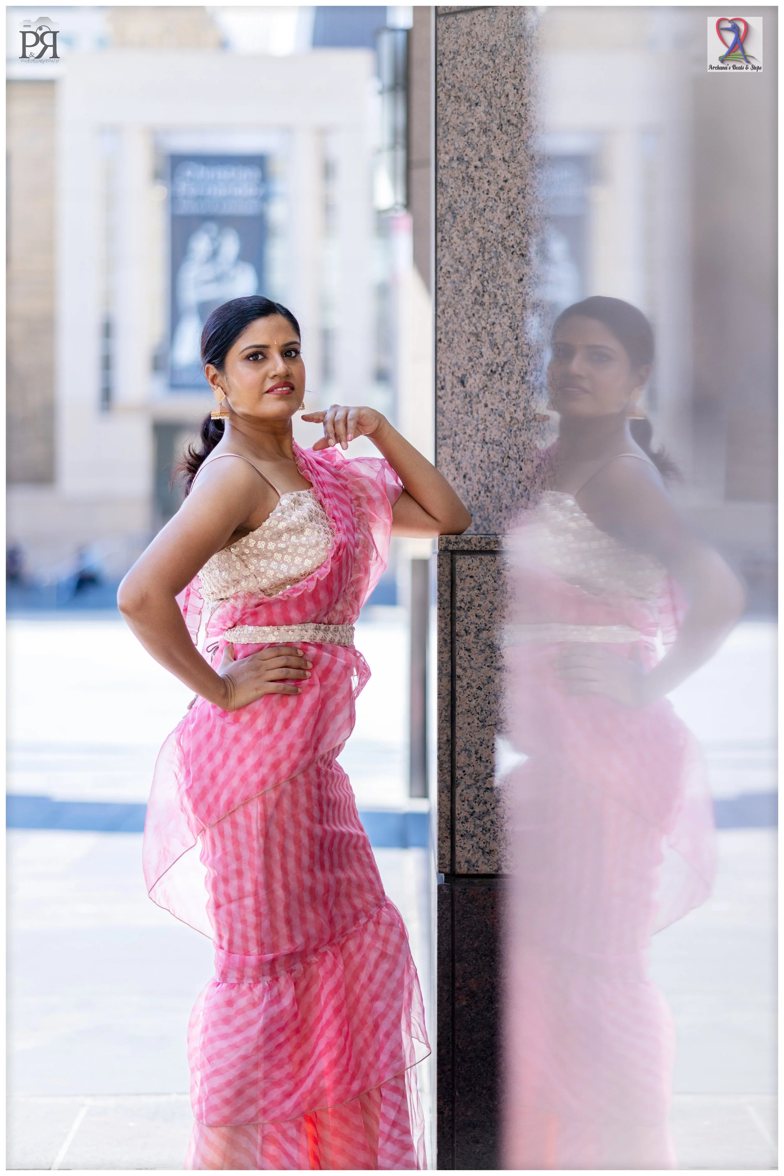 Woman wearing pink and white traditional Indian attire posing near a reflective glass wall