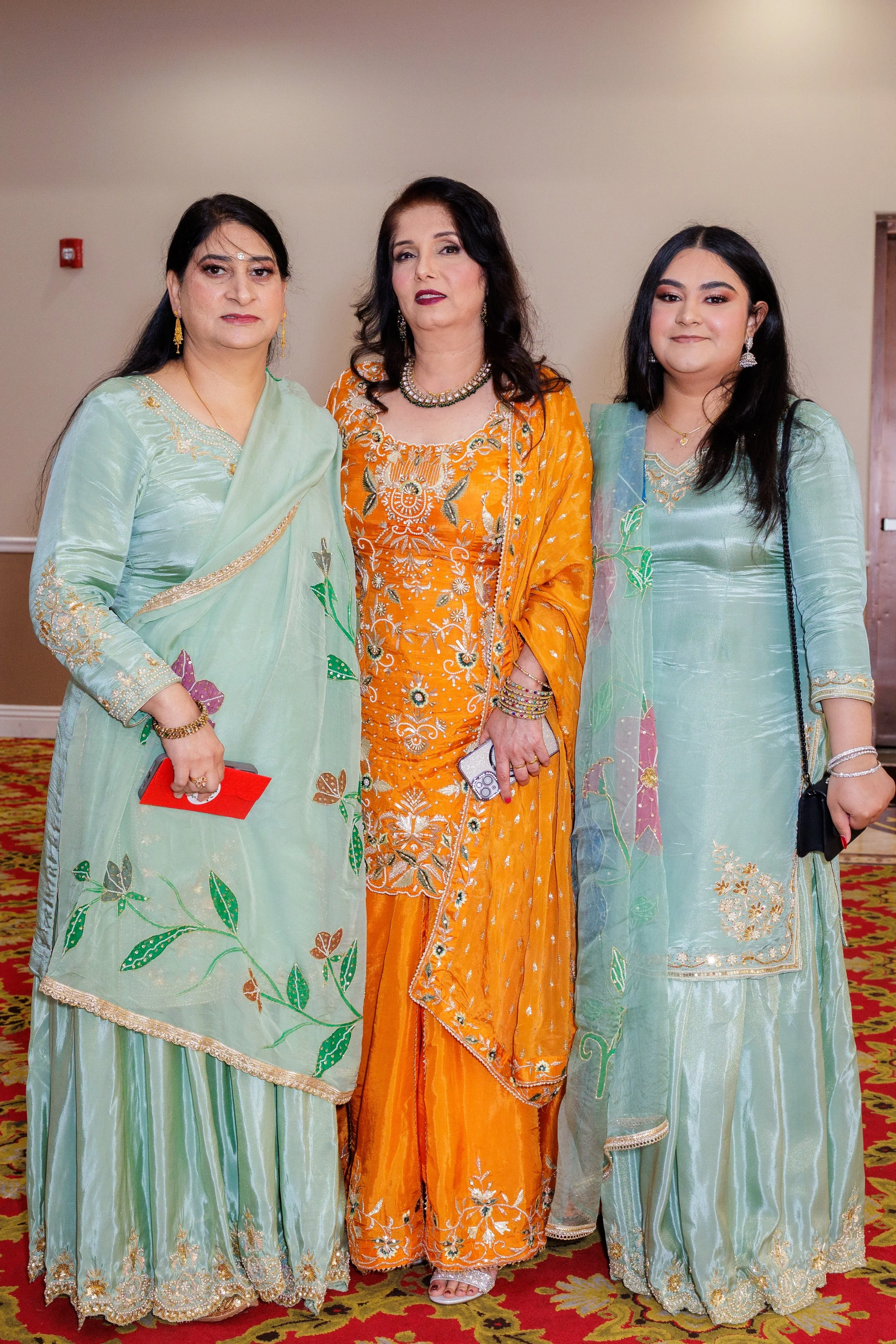 Three women dressed in colorful traditional Indian attire posing indoors on a patterned carpet
