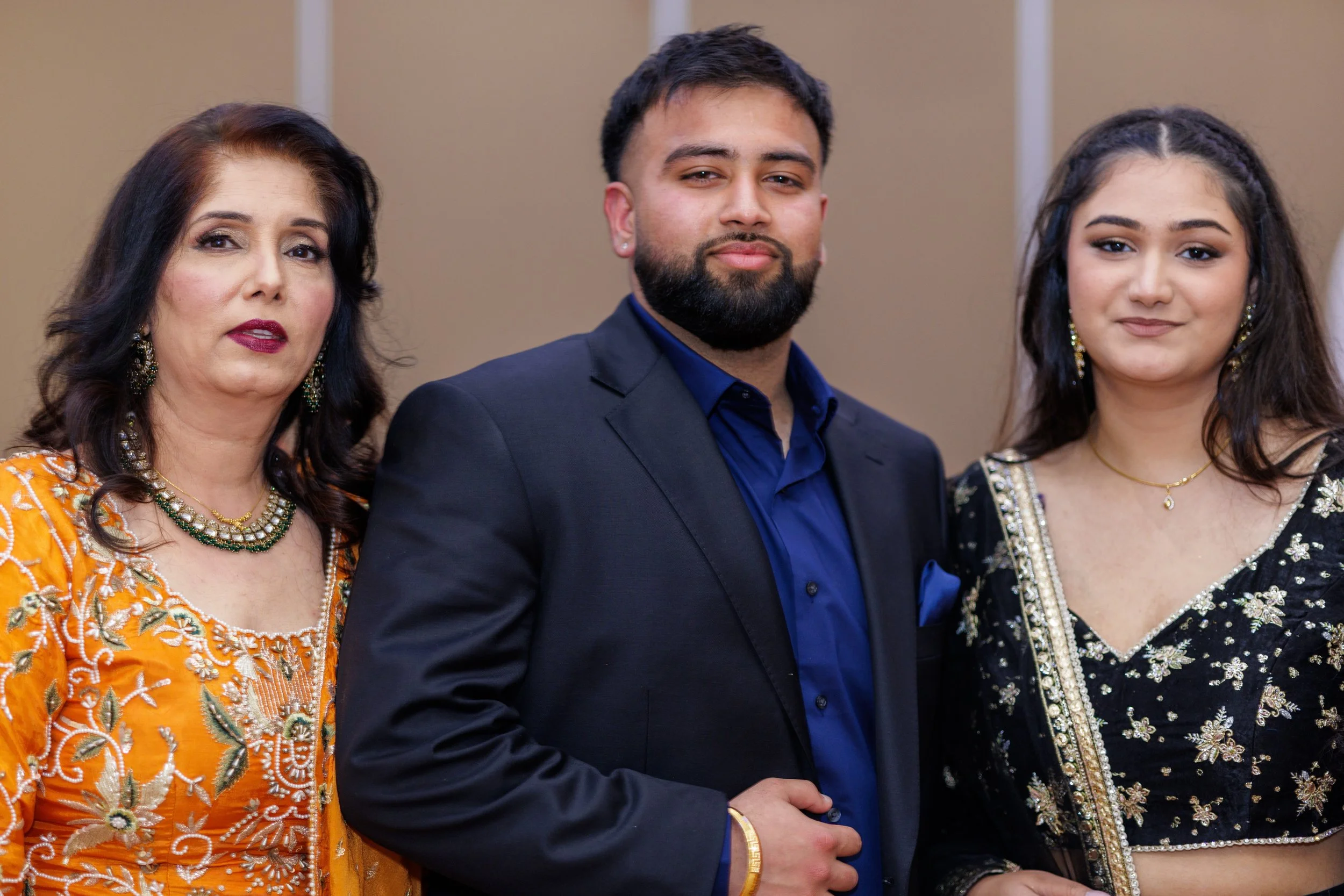 Three people standing together at an event, dressed in formal and traditional attire, with neutral background.