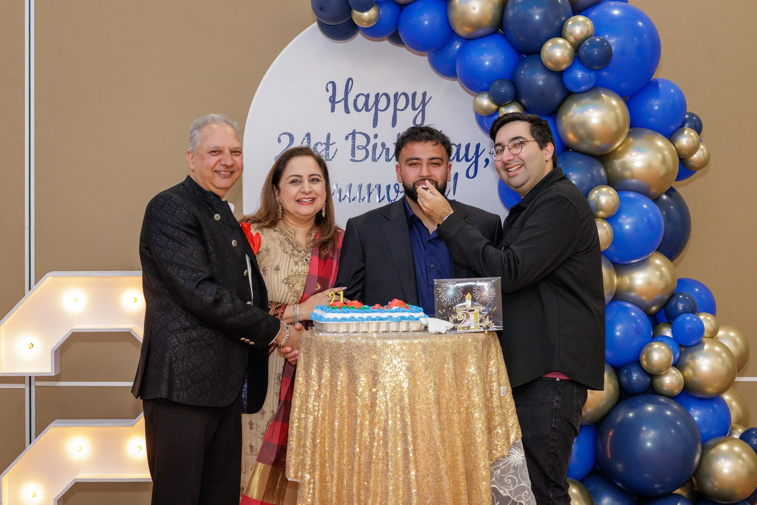 Family celebrating 21st birthday with cake, balloons, and a decorated backdrop.