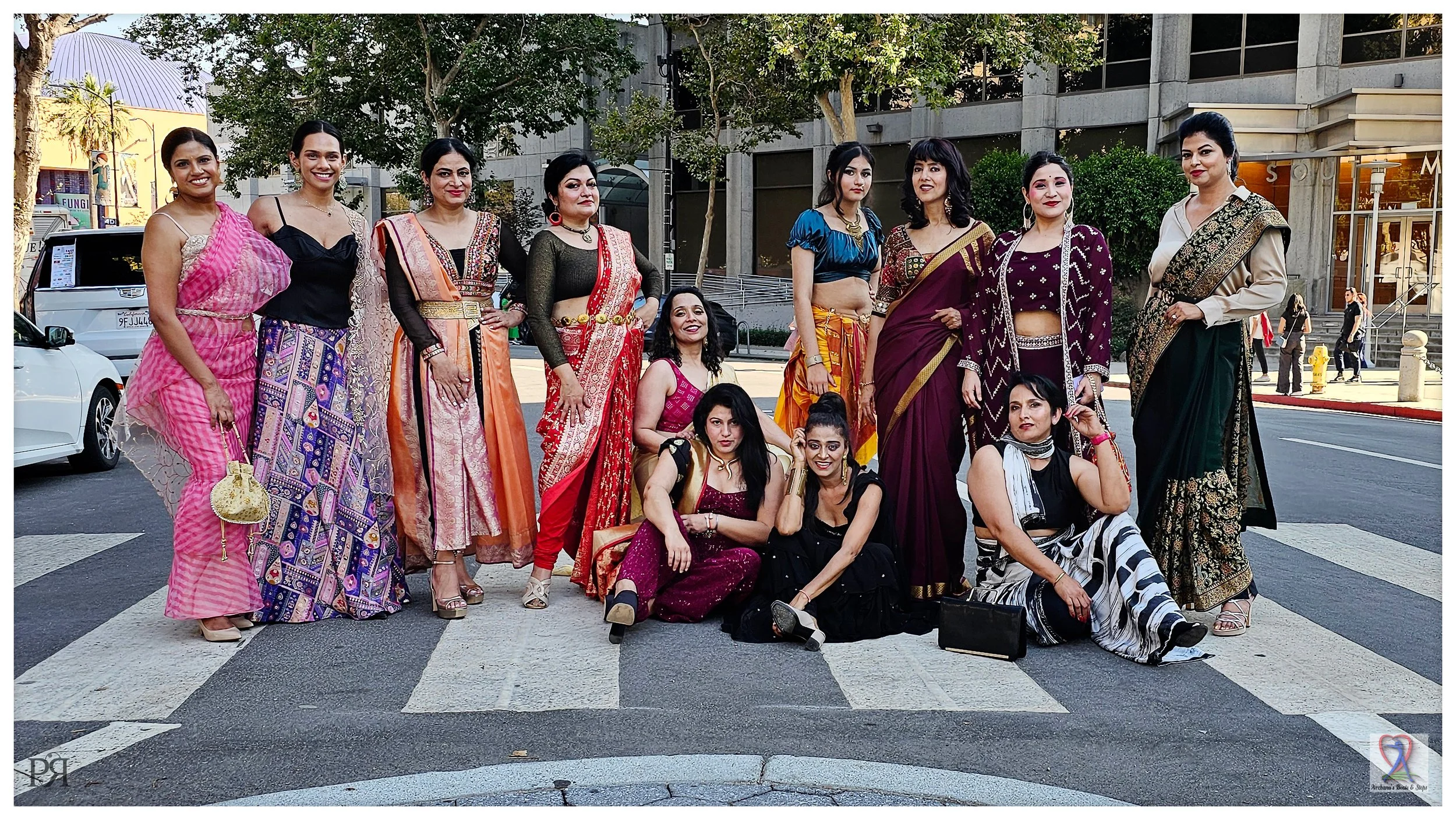 Group of women in colorful traditional Indian attire posing on a street crosswalk.