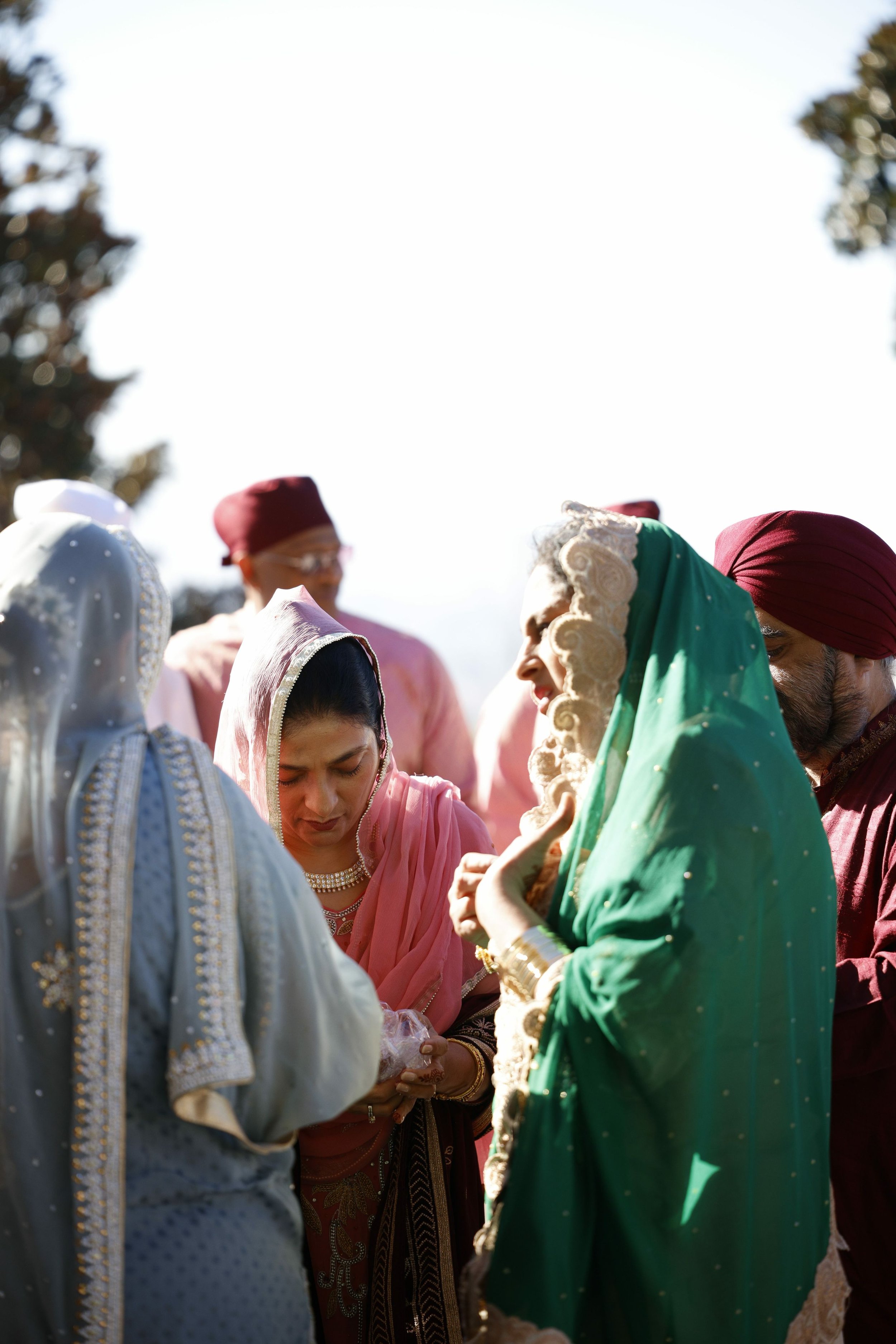 Indian wedding ceremony with women and men dressed in traditional colorful attire, standing outdoors.