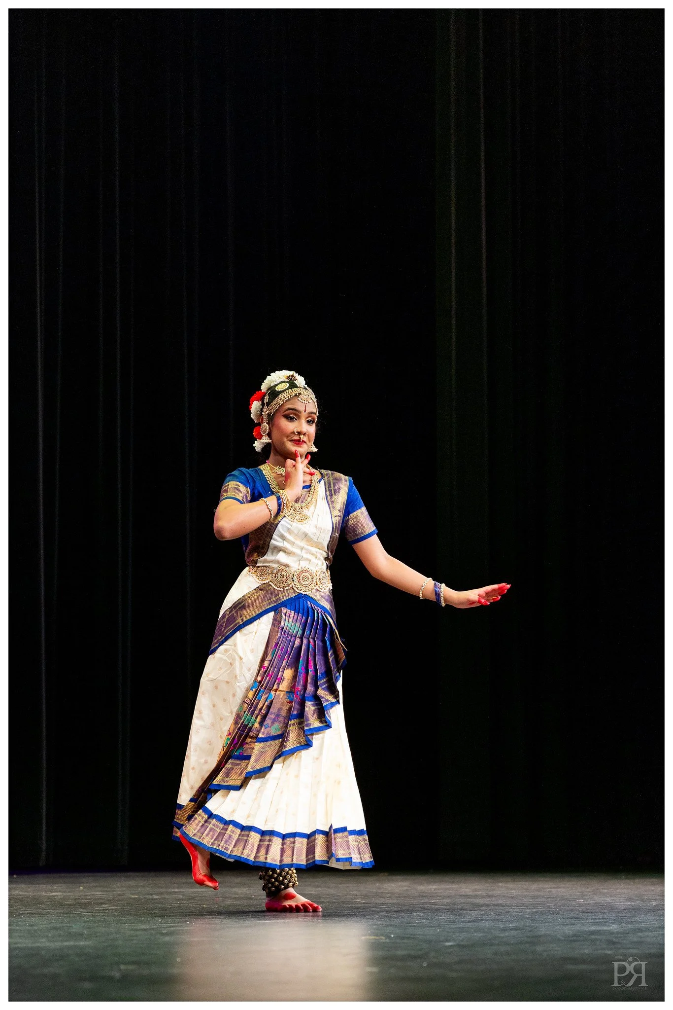 A woman performing a traditional Indian dance in colorful attire on stage with a black background.