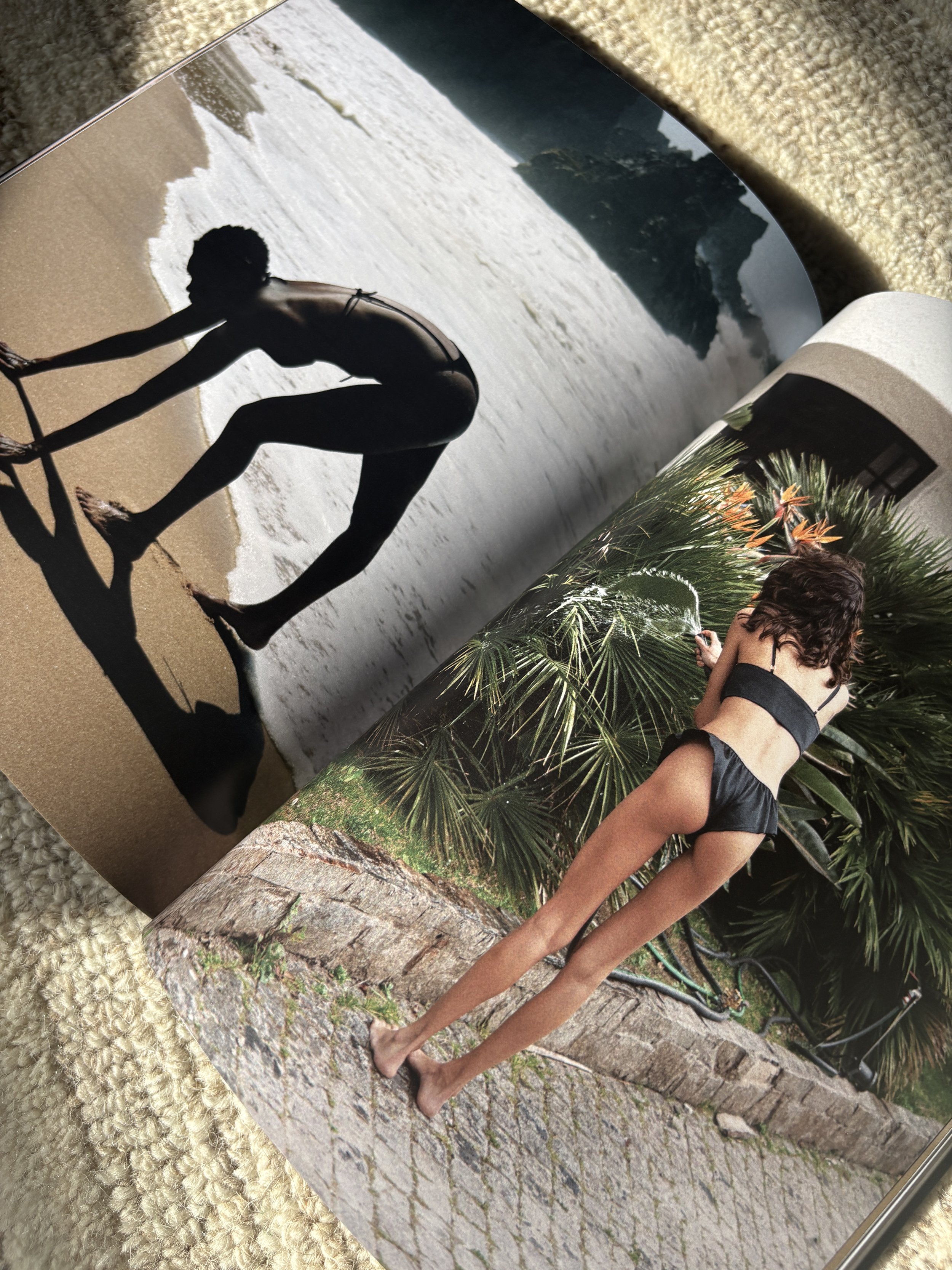 A person stands outdoors on a cobblestone path, surrounded by lush greenery and tropical plants. The individual is dressed in black shorts and a black top, and appears to be looking down at the ground.