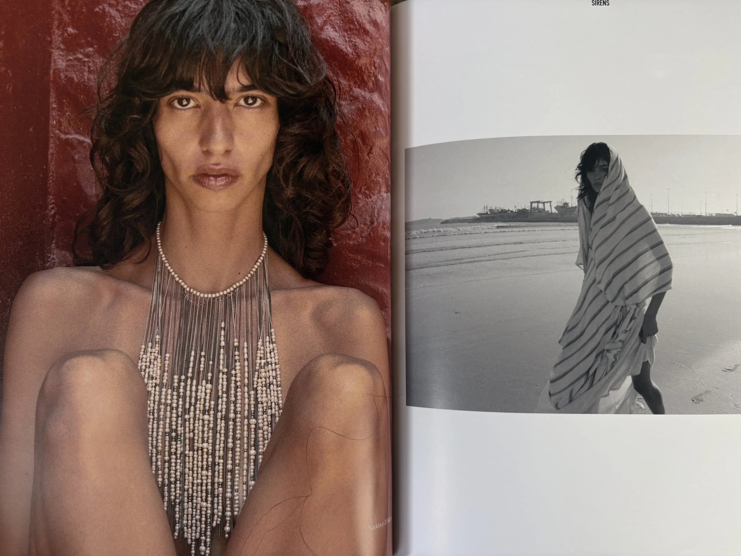 A color photograph of a woman with dark, curly hair and brown eyes, standing against a textured red wall. She is wearing a layered pearl necklace and has a serious expression. The adjacent black-and-white photograph shows the same woman at the beach,