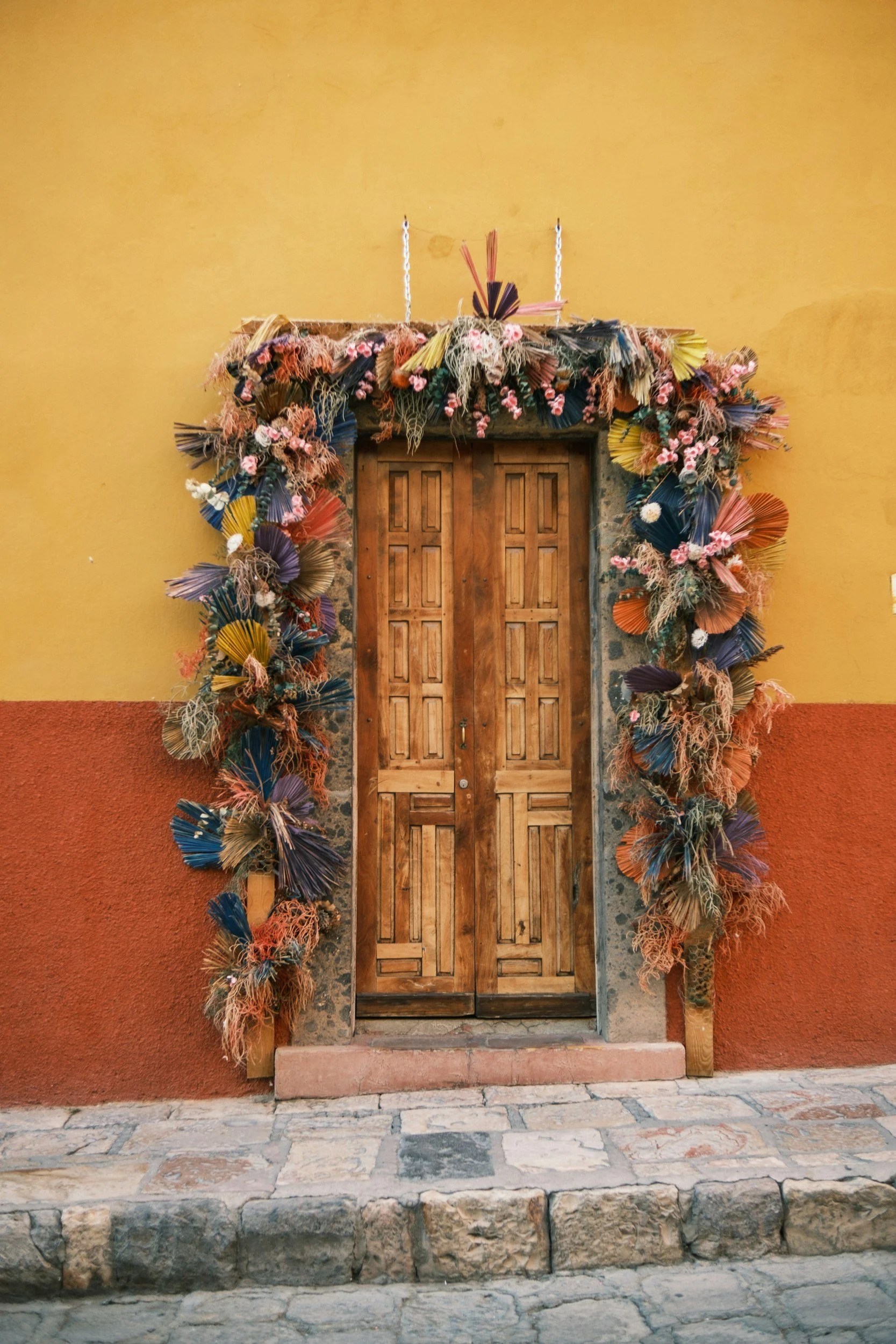 Wooden door framed by a colorful dry floral arrangement on a yellow and red painted wall.
