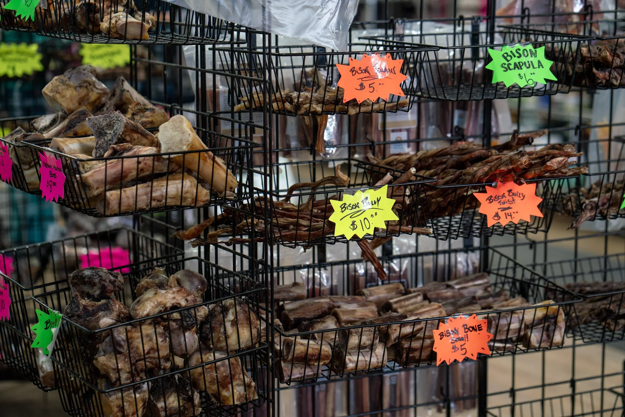 Baskets of various dried meats and animal bones with colorful handwritten price tags at a market stall.
