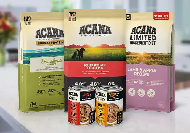 Several bags of Acana dog food and two cans of Acana dog food in front of the bags, with a blurred background.