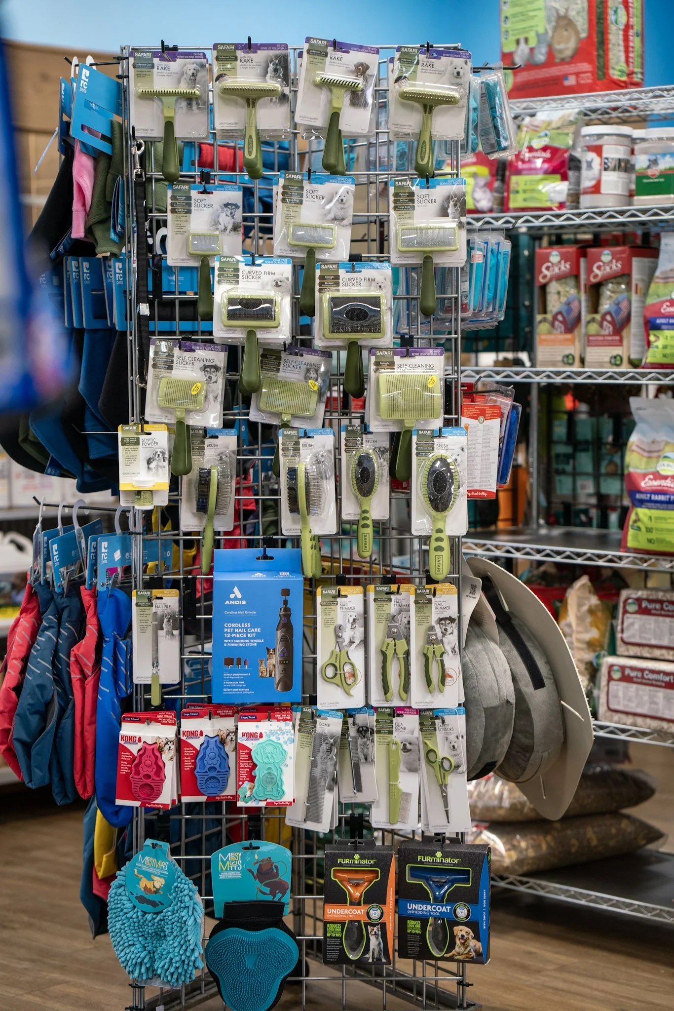 Display of pet grooming tools including slickers, brushes, nail trimmers, and de-shedding tools in a pet supply store.