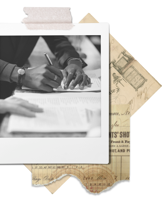 A person signing documents at a desk, with a calculator and older paper documents underneath.