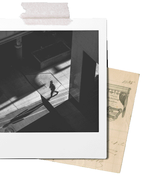 A black-and-white photo taken from a building window shows a person walking on the sidewalk outside. There is a shadow cast on the sidewalk, and a section of the building's interior is visible.