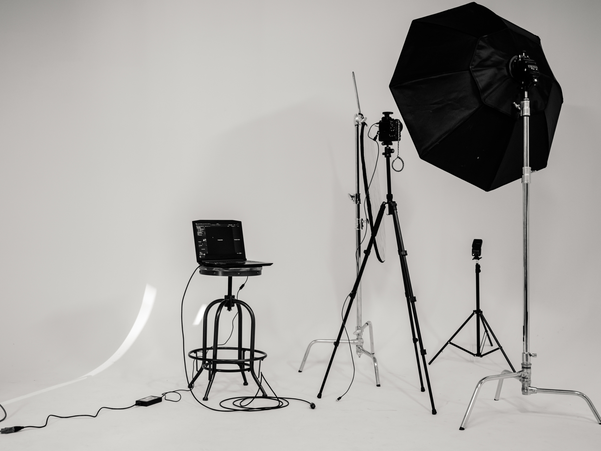 Photography studio setup with lighting equipment, a laptop on a stool, and a white background.