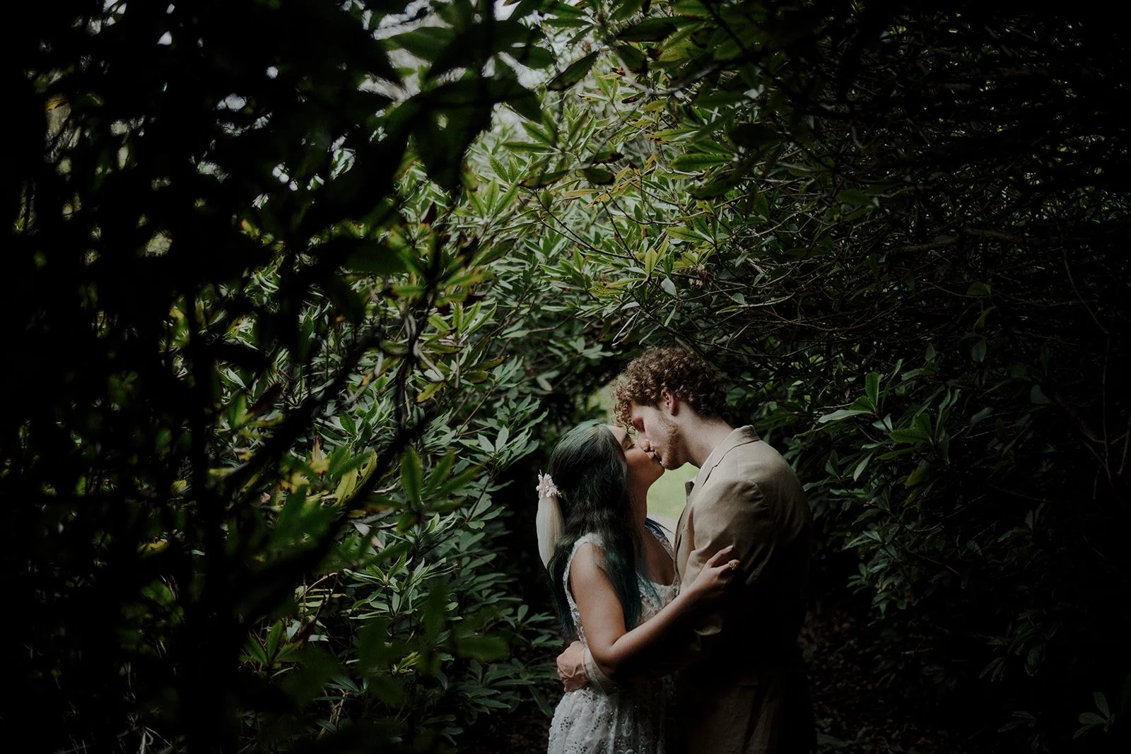 A photograph of a couple enjoying a moment by themselves in a forest in the netherlands while they are basking in the light trickling in through the trees