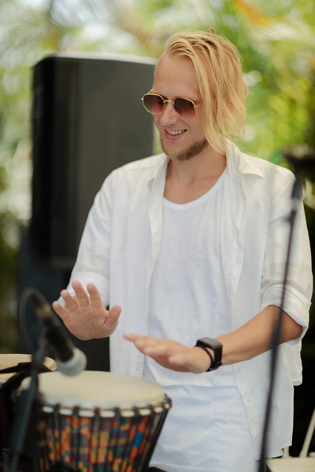 A photograph of a drummer with greens in the background and a smile on his face