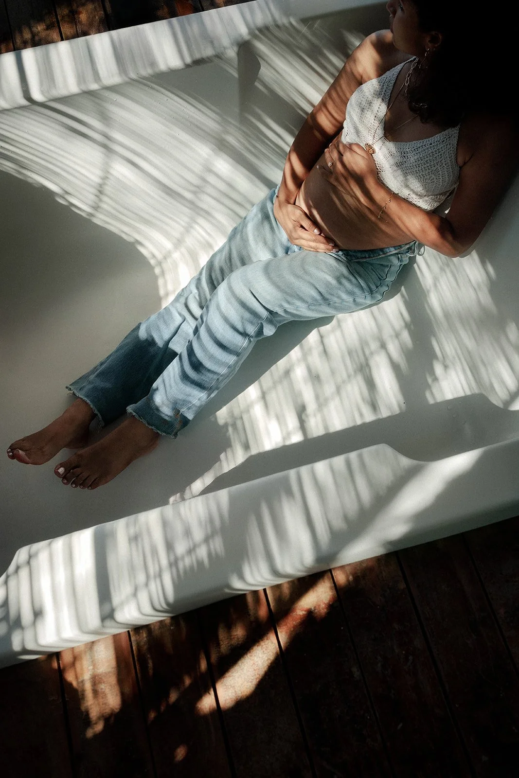 A maternity photograph of a lady in a tub with lovely shadows of the trees cast on her body