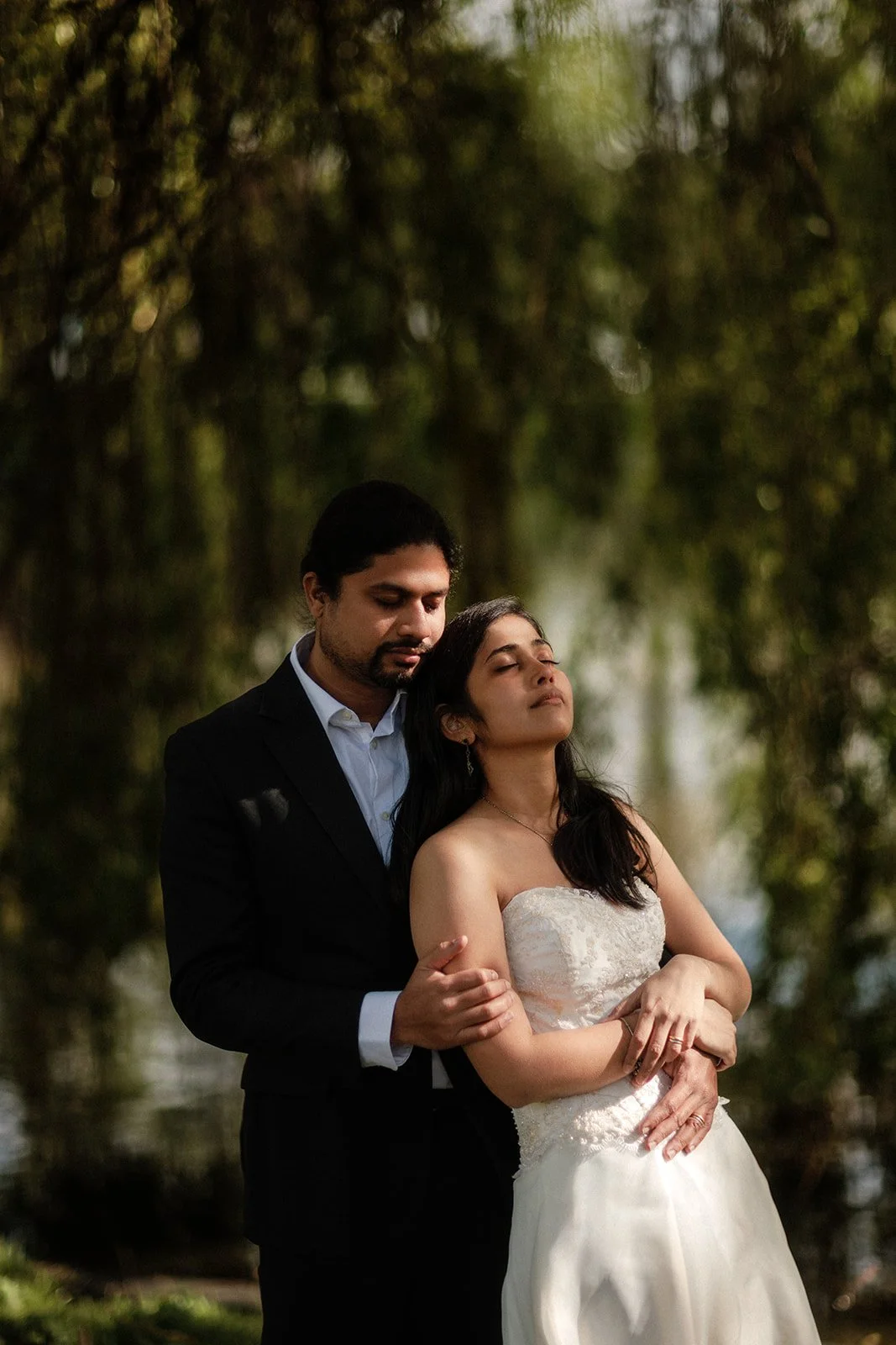 A photograph of a bride resting her head on the grooms shoulder as the sun shines on her in Groningen