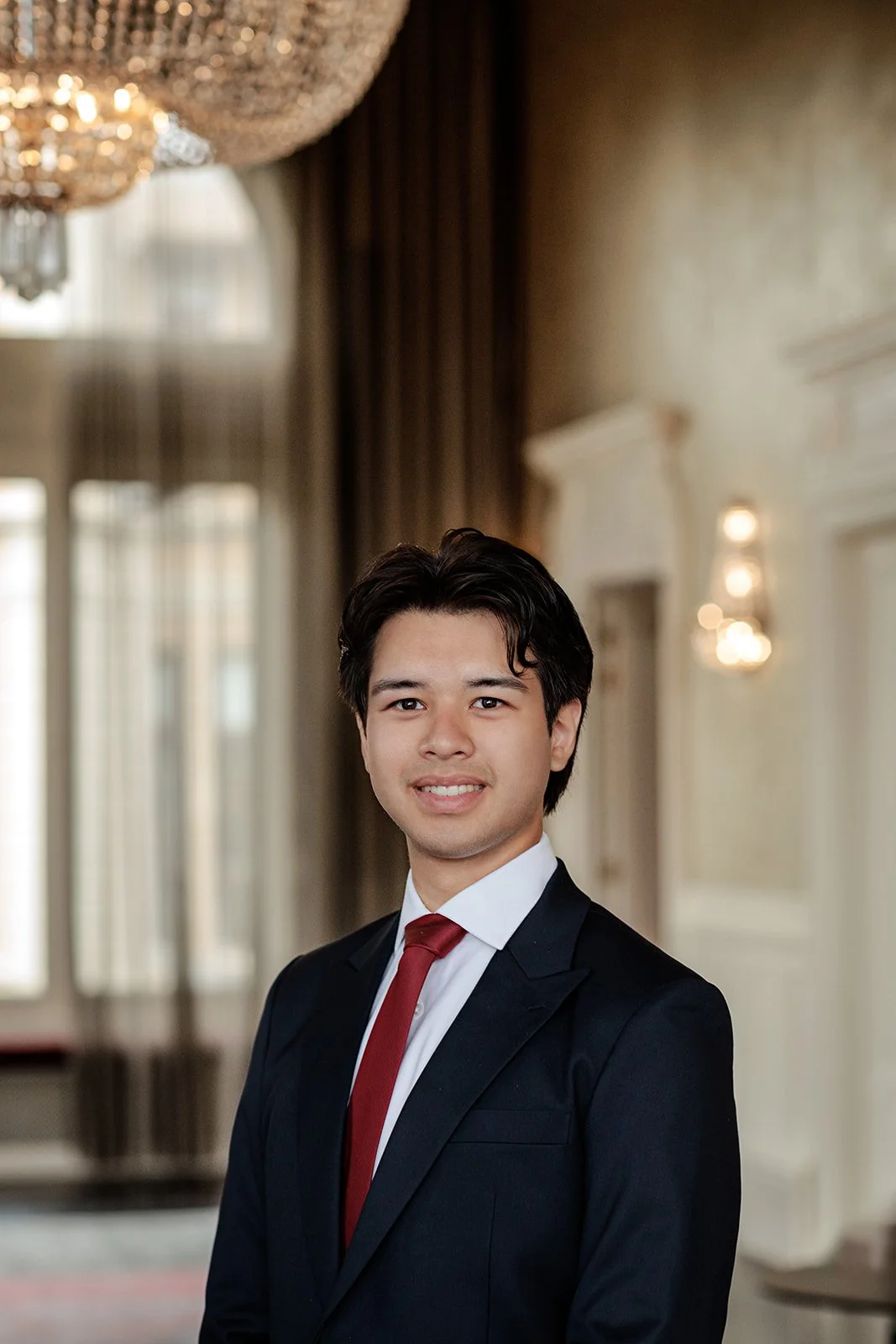 A headshot portrait photograph of a man with black hair in blue suit and a red tie shot by Darius N Fernandes