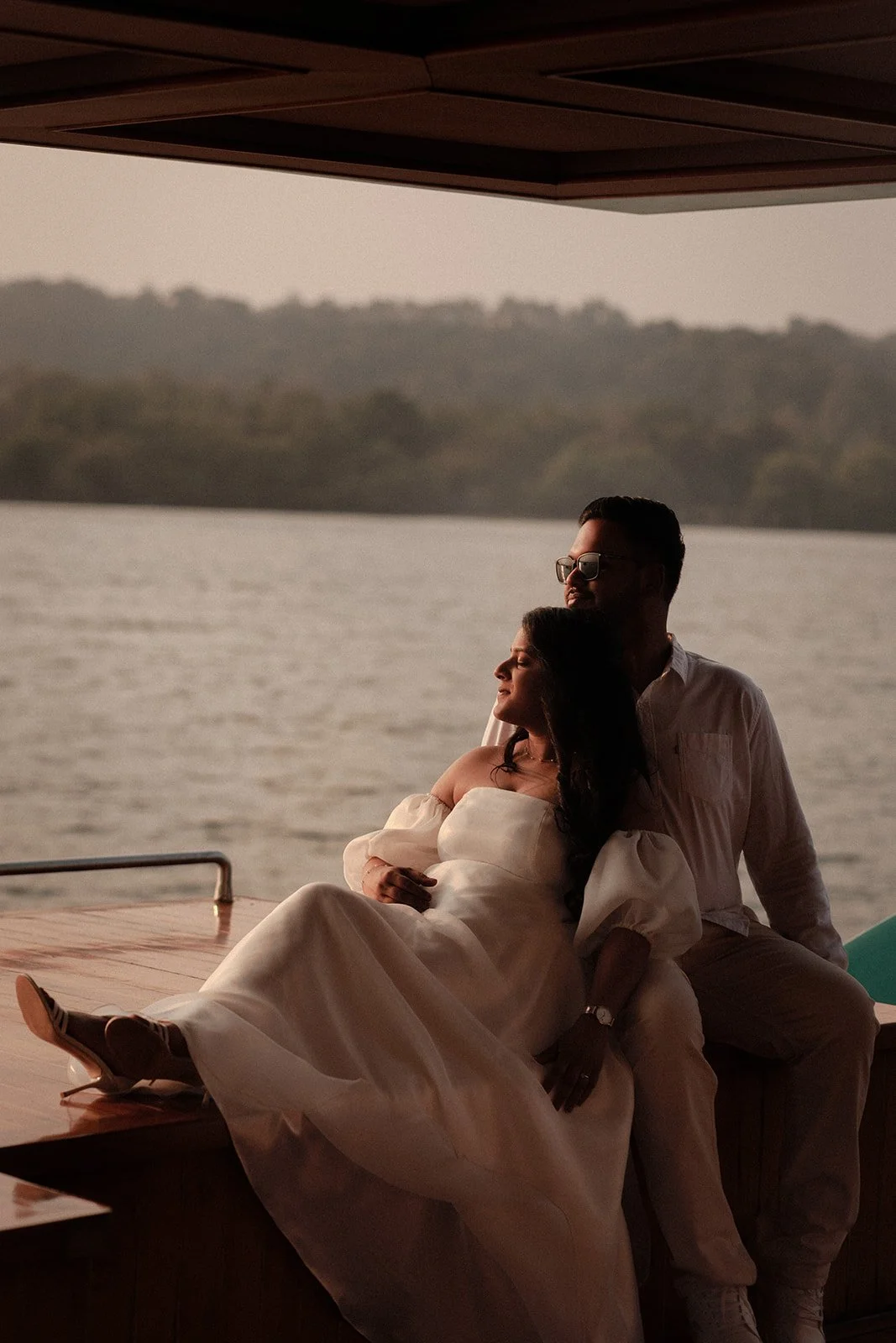 A photograph of a couple at a party basking in the sunlight on a boat with the sea in the background