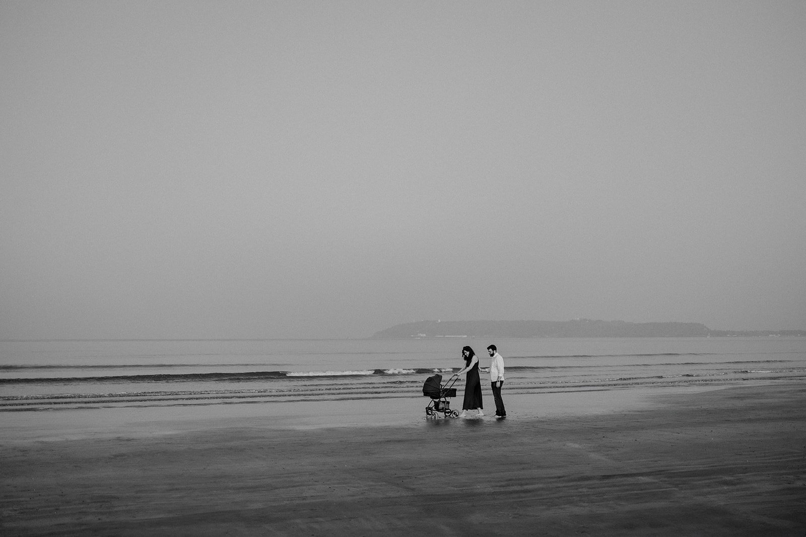 A black and white family photograph of a couple pushing a stroller on a beach 