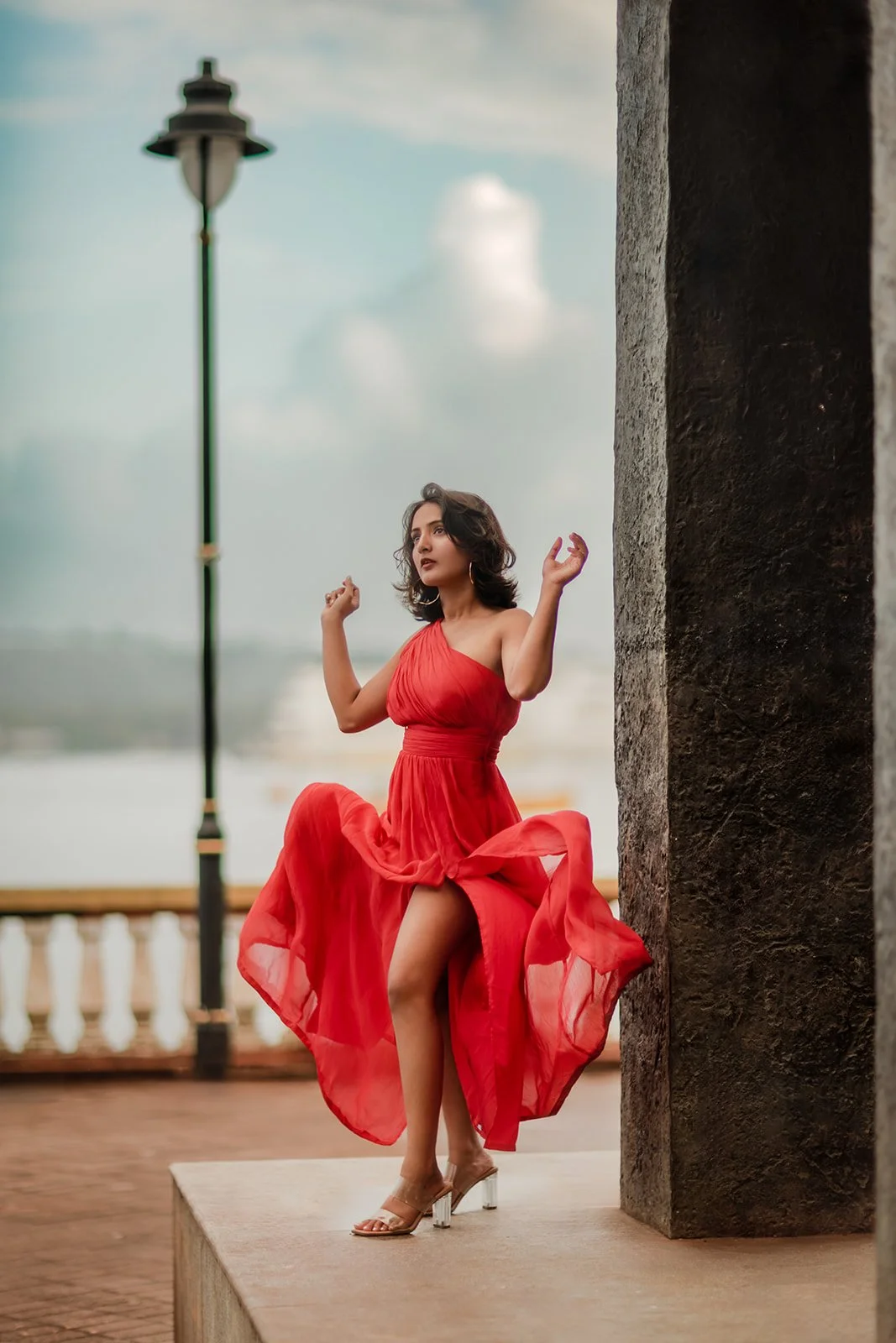 A portrait of a girl in a red dress with her dress blown in the wind with blue clouds in the background 