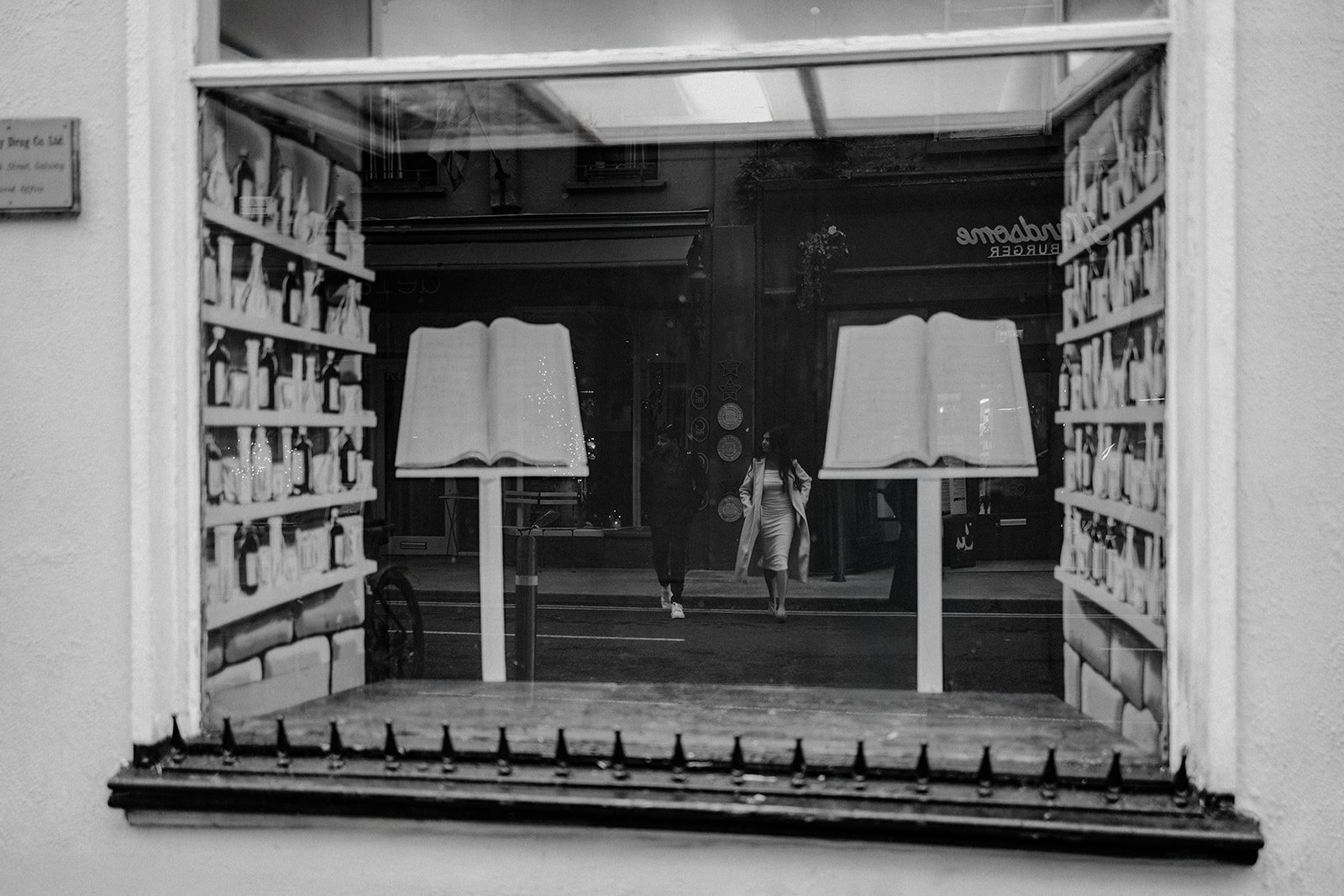 A photograph of a couple walking down the street taken through a reflection of a book stores glass 
