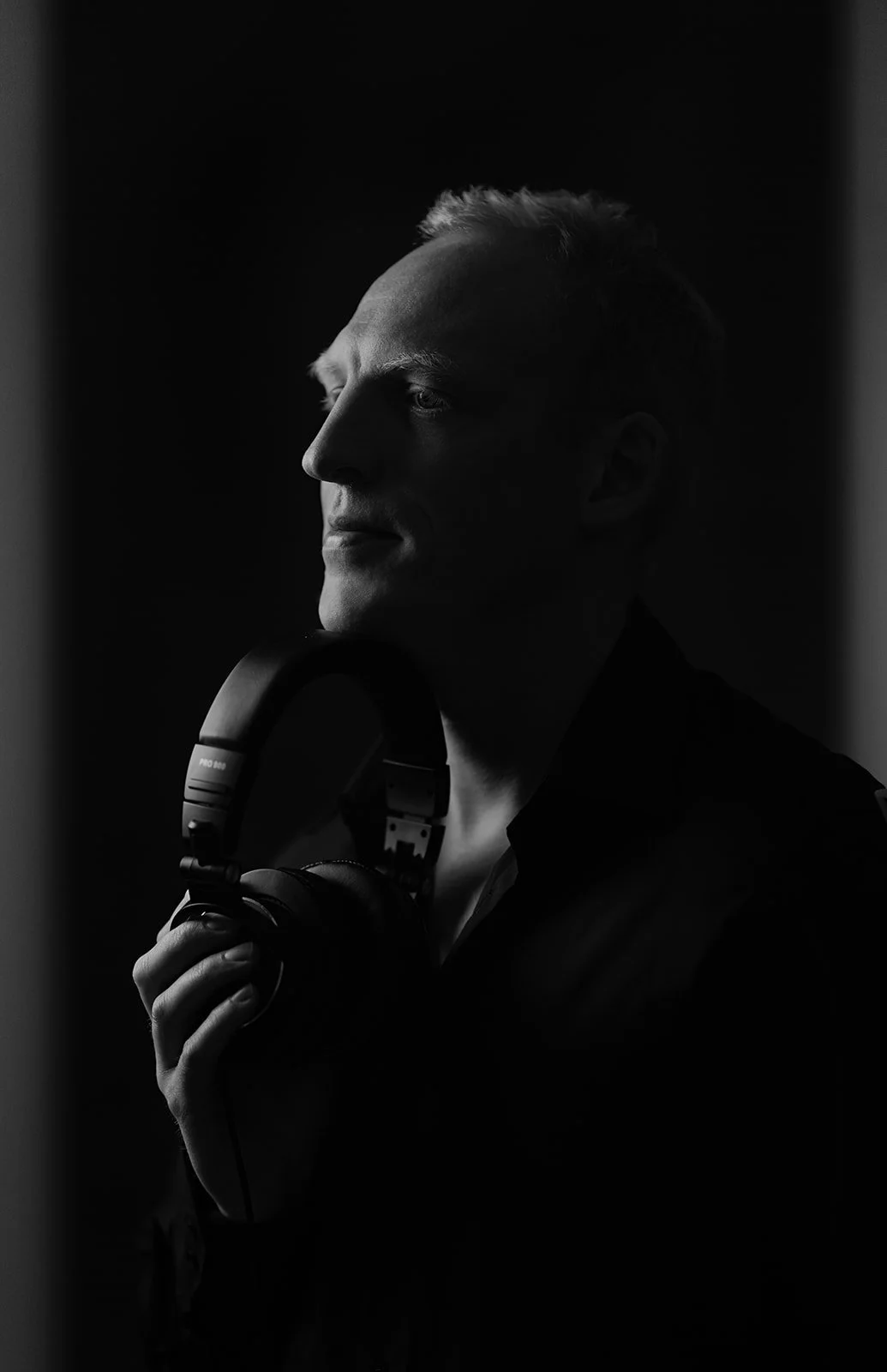 A black and white portrait of a DJ with his headset in his hands staring into the distance 