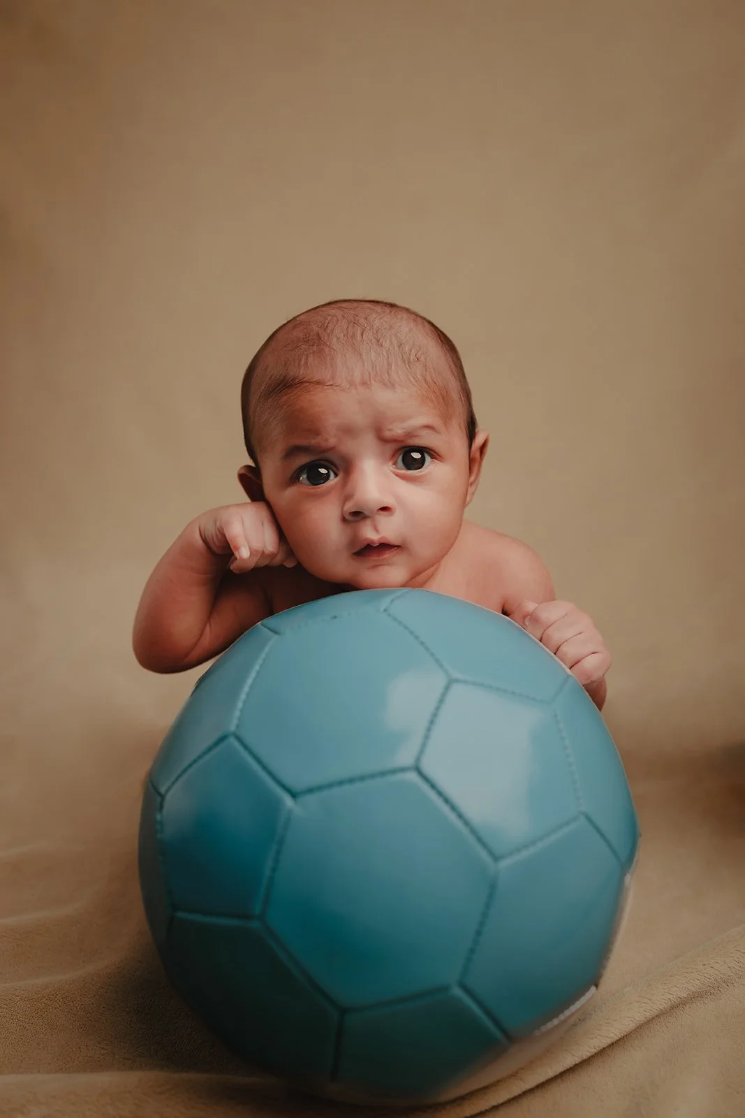 A new born photograph of a child looking straight into the camera while resting on a football