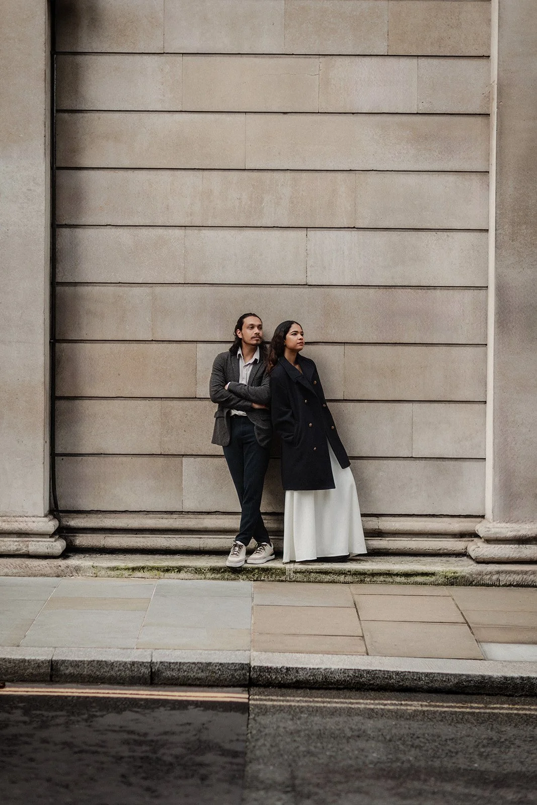 A bride and groom both with a coat on posing by an old dutch wall 