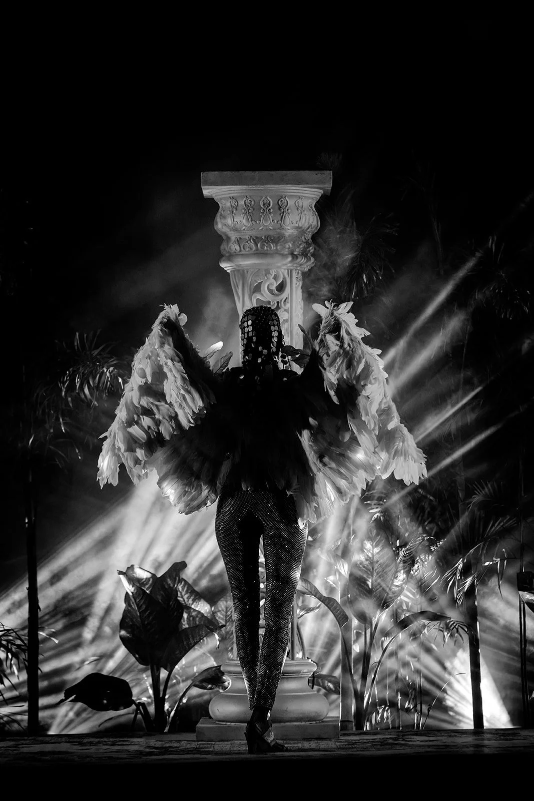 A Black and white photograph of a model walking down a runway for an event she is wearing a shimmering costume with wings