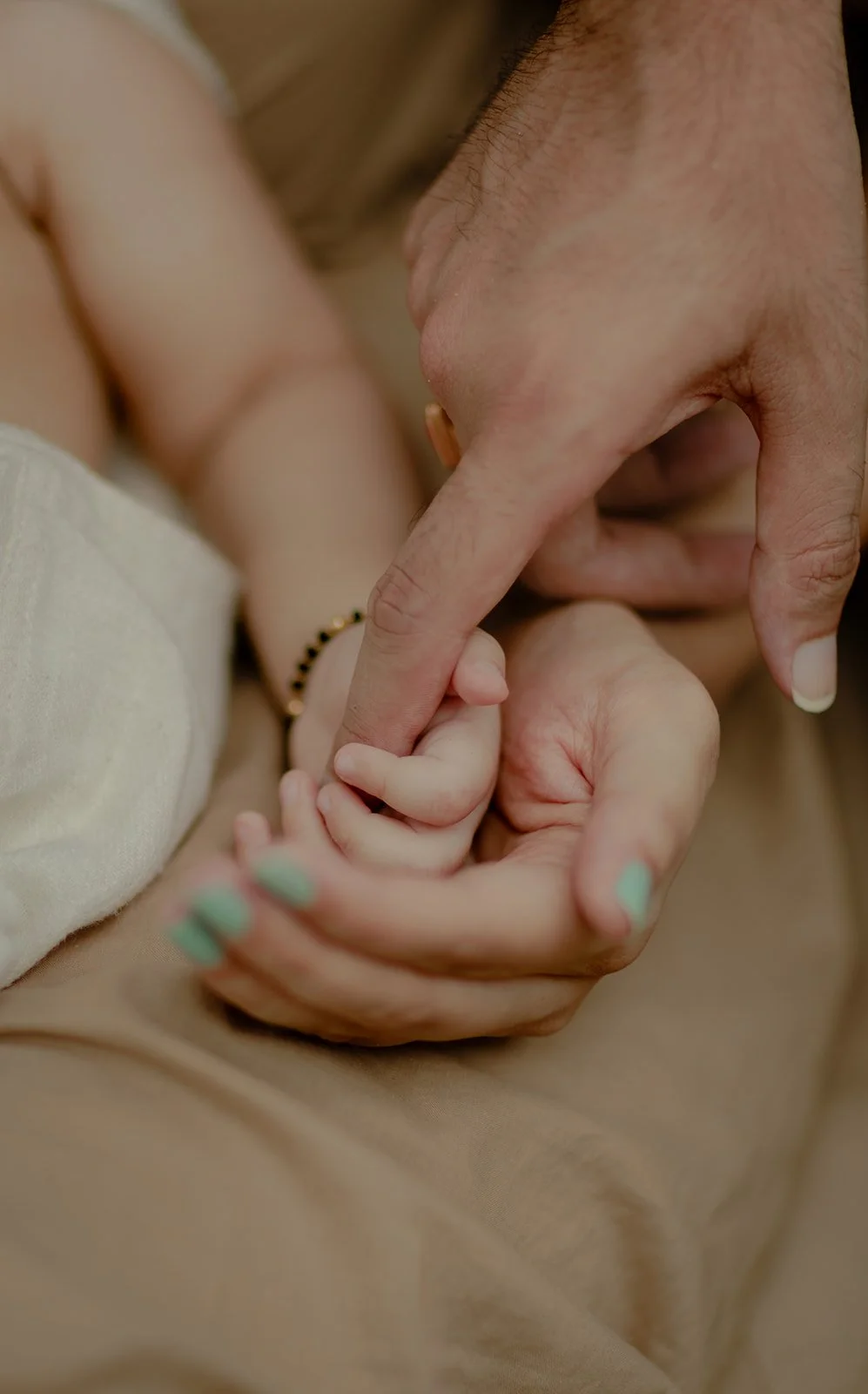 A family portrait taken by Darius N Fernandes where in the child is holding on to the fathers finger while the mother is cupping the child's hand