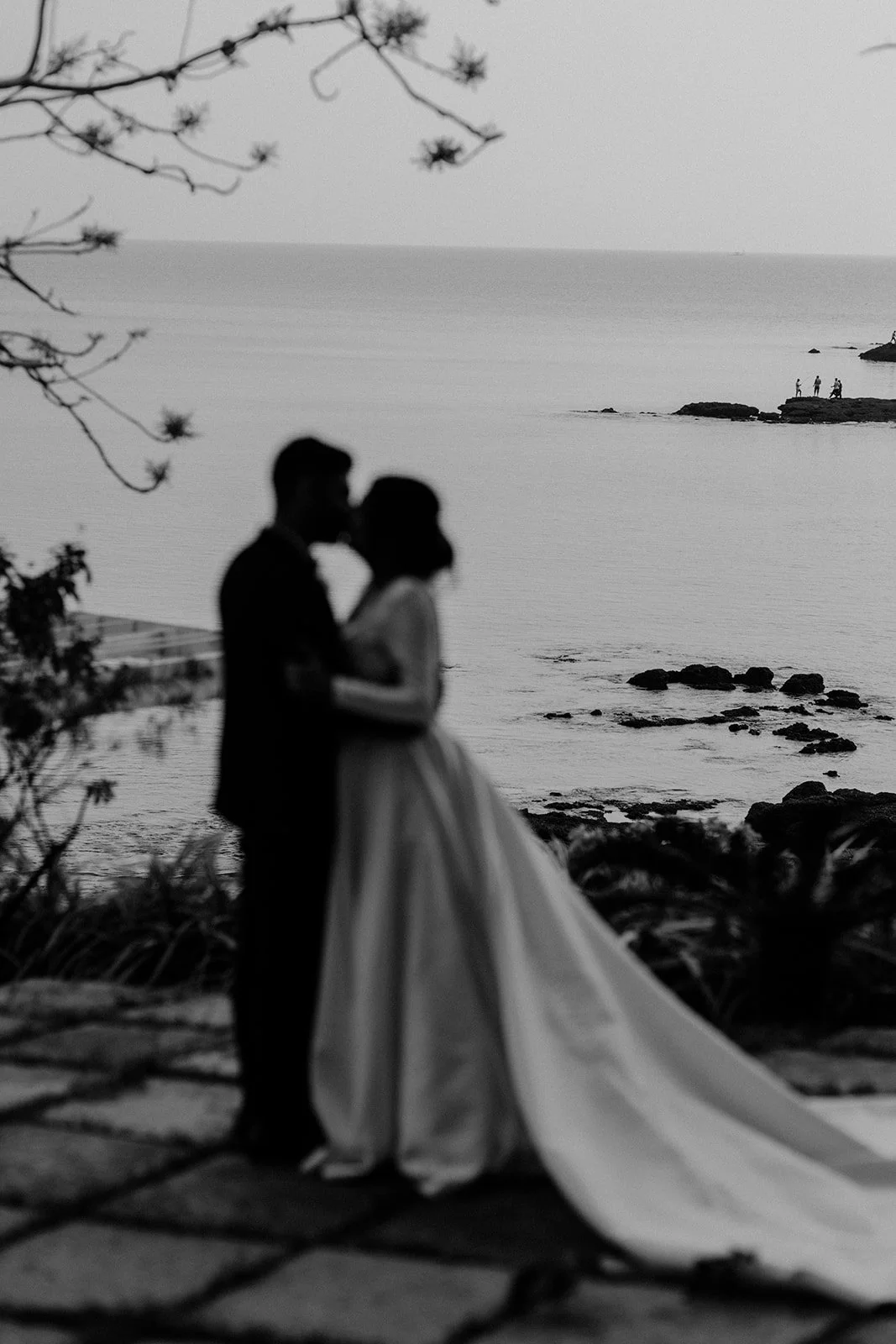 A black and white picture of the bride and groom kissing with the sea in the background