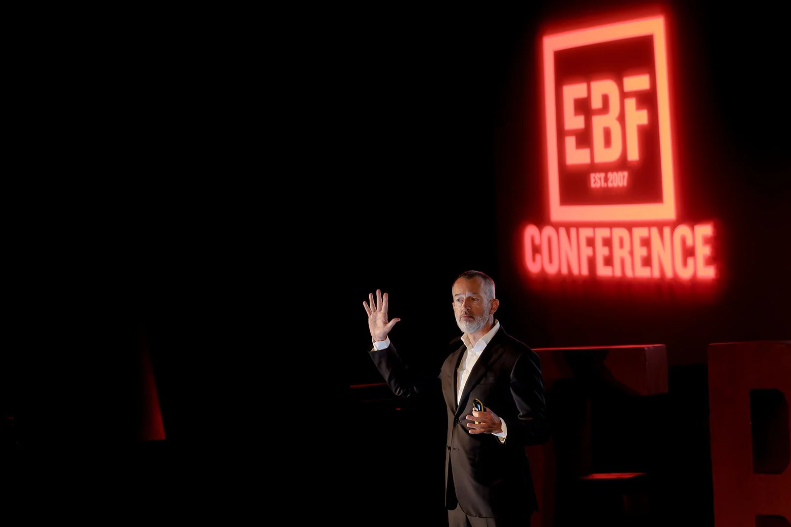 Event photography of a man talking to the crowds with a red sign in the background