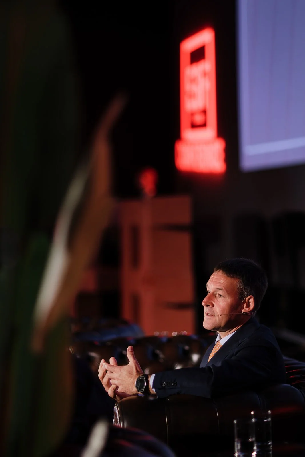 An event photograph of a man on stage explaining to an audience